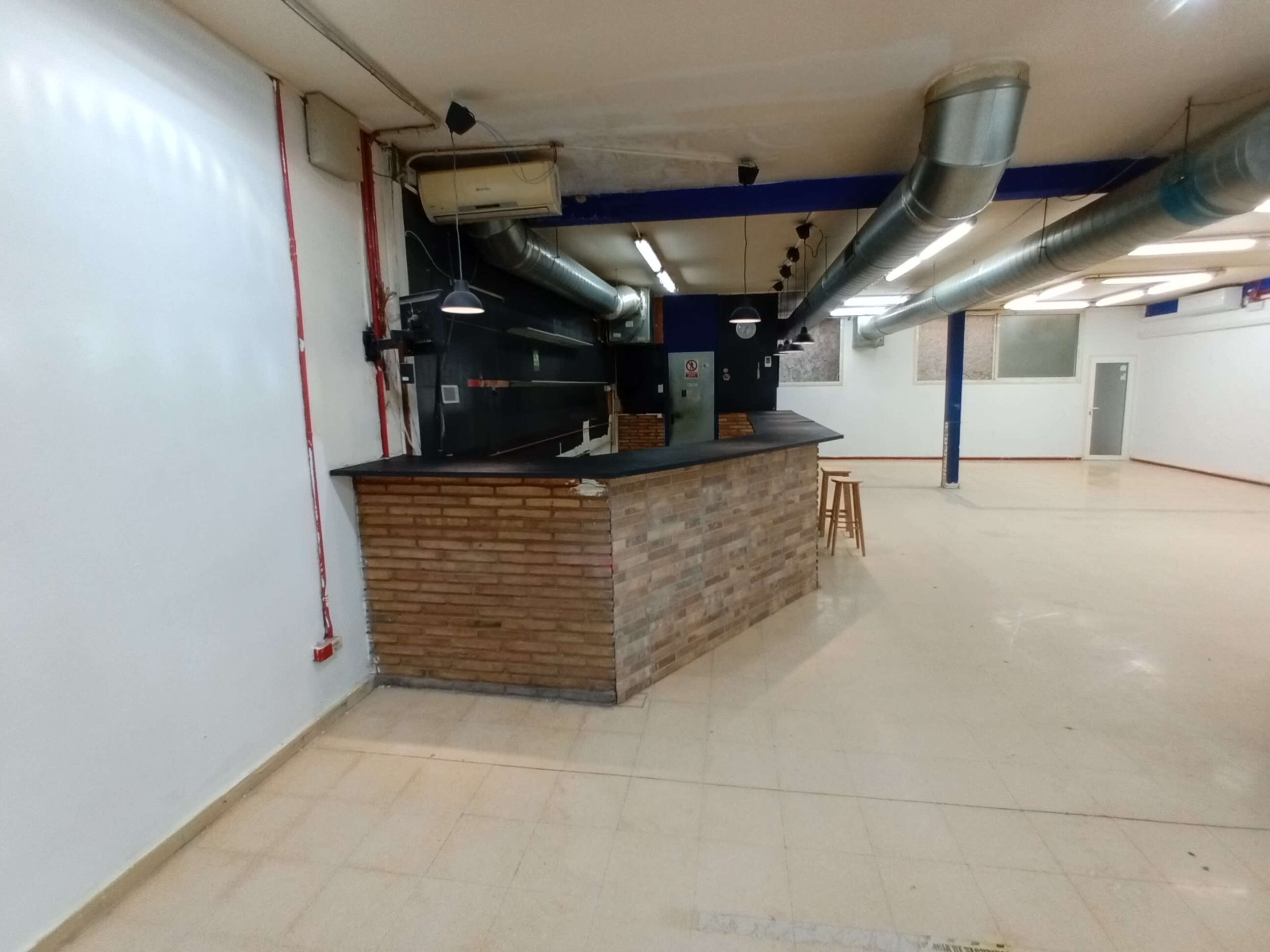 The image shows a spacious, empty interior featuring a brick-clad counter and exposed ductwork on the ceiling.