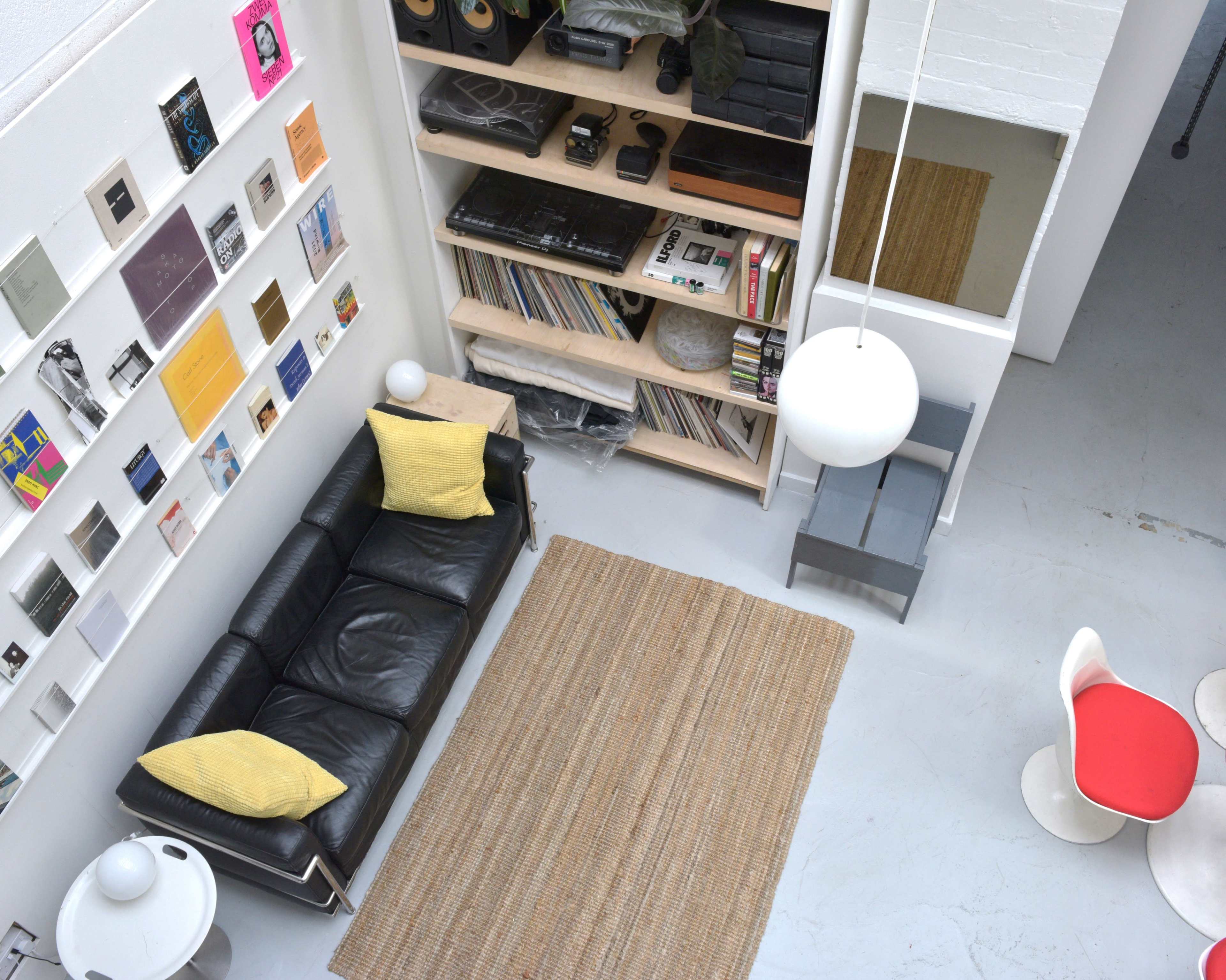 A modern living space featuring a black leather sofa, a light-colored rug, and a wall adorned with various framed artworks and vinyl records.