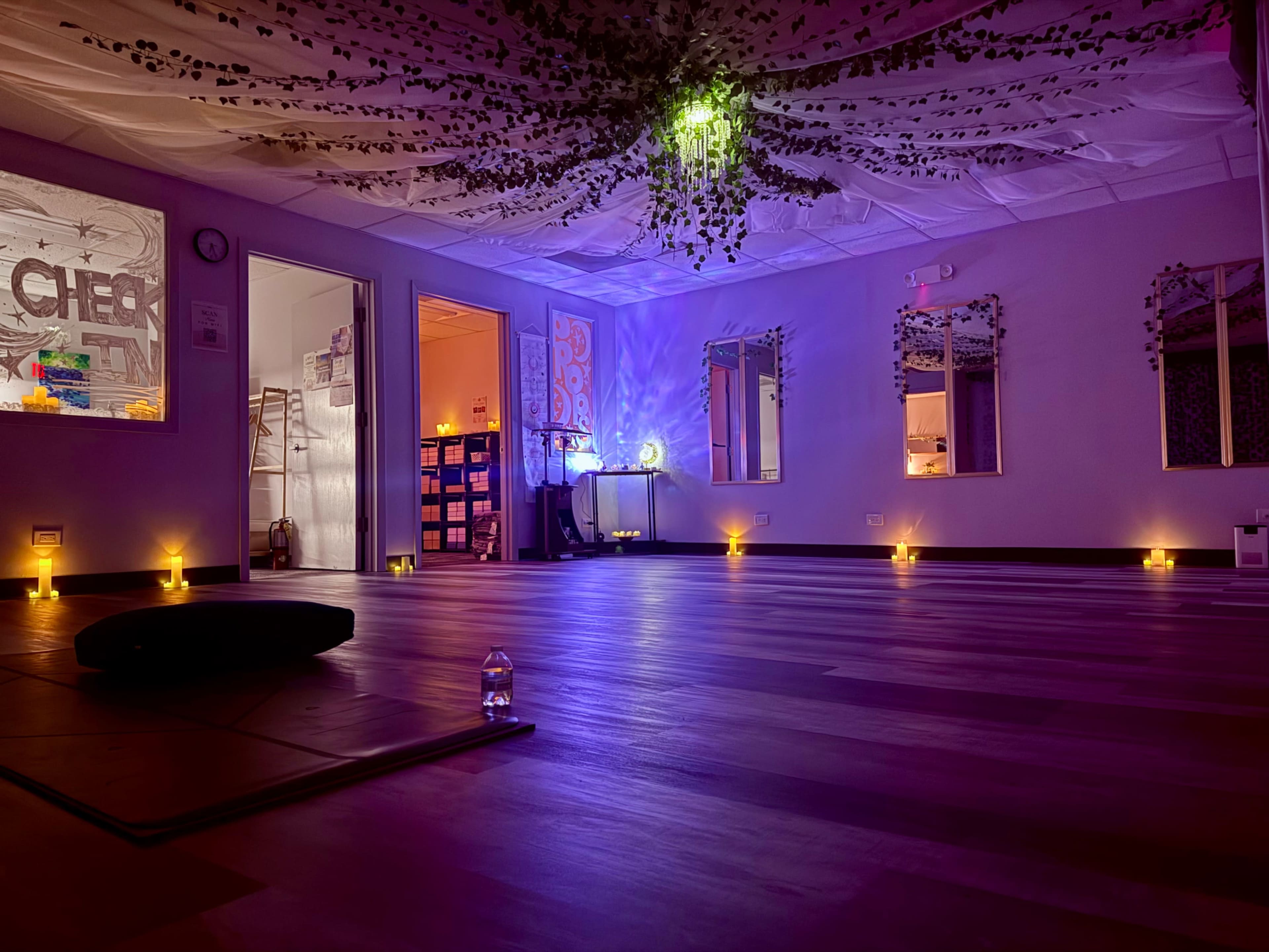 The image shows a softly lit yoga studio with candles and decorative plants, creating a serene atmosphere.