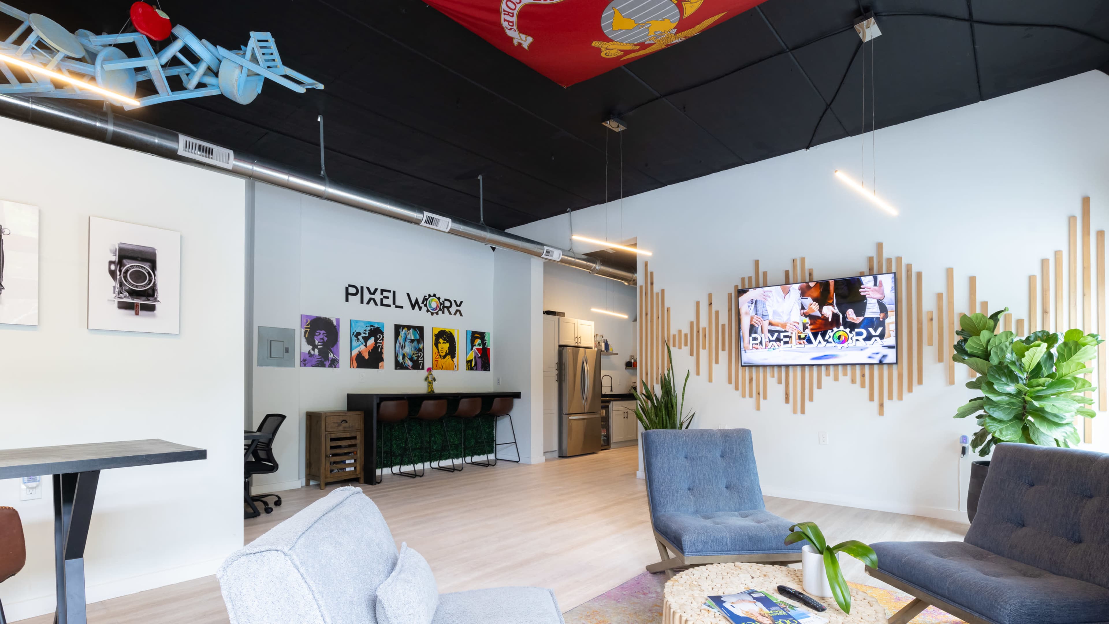 A modern office space with comfortable seating, a television displaying "PIXEL WORX," and decorative wall elements.