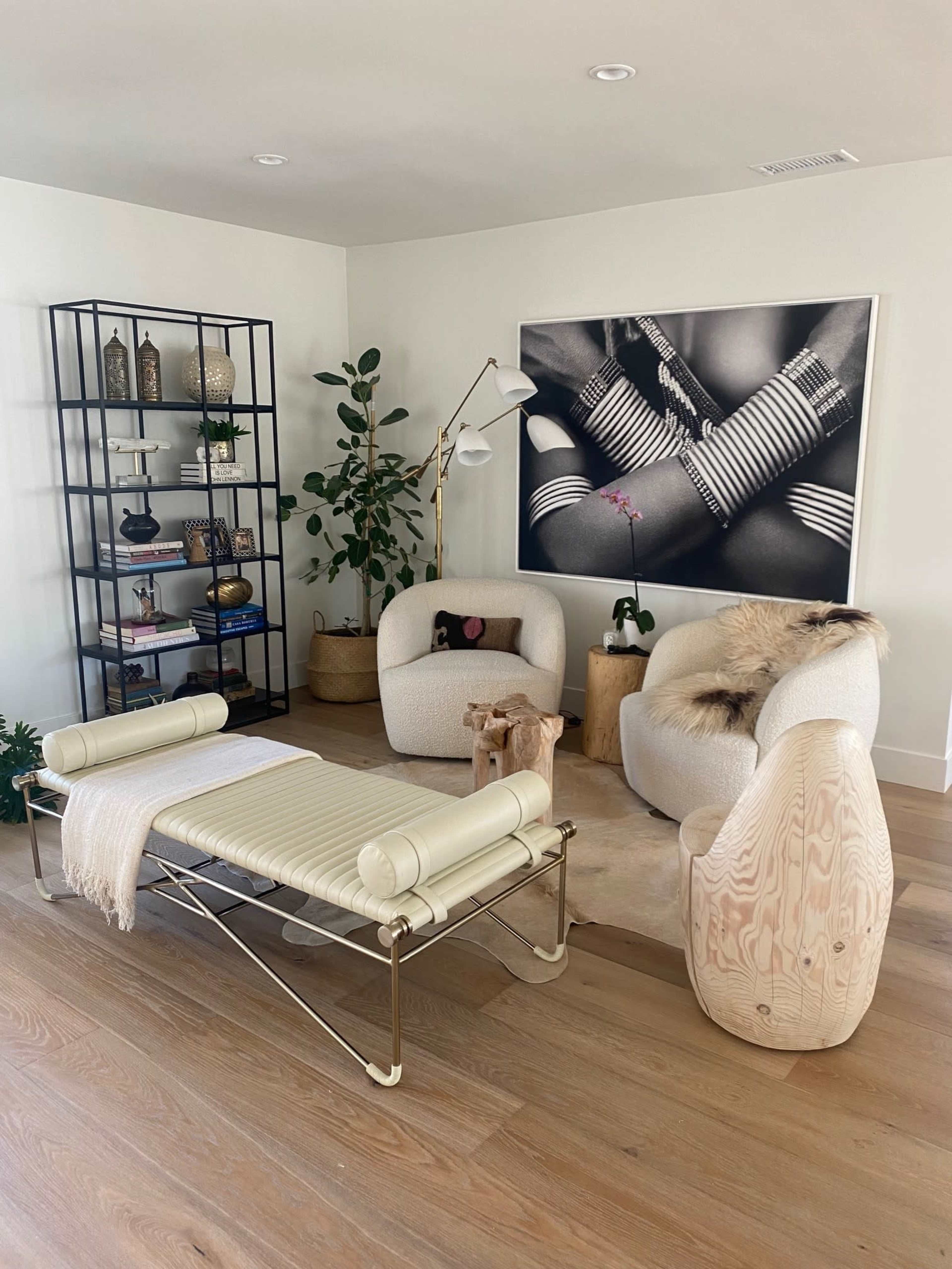 A modern living room with two upholstered chairs, a bench, and a bookshelf, featuring decorative items and a large black and white photograph on the wall.