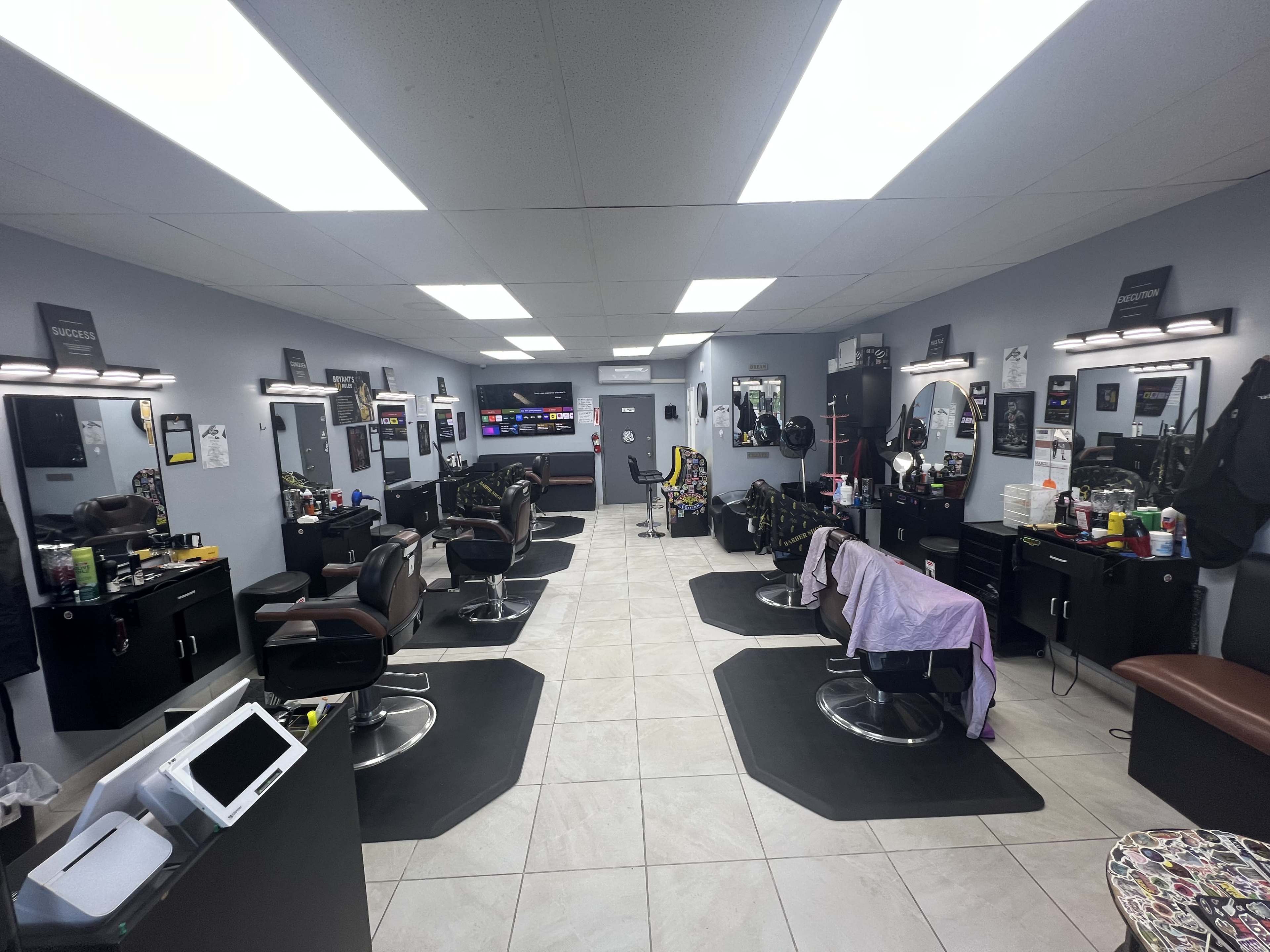 The image shows a modern barbershop interior with multiple barber chairs, styling stations, and a reception area.