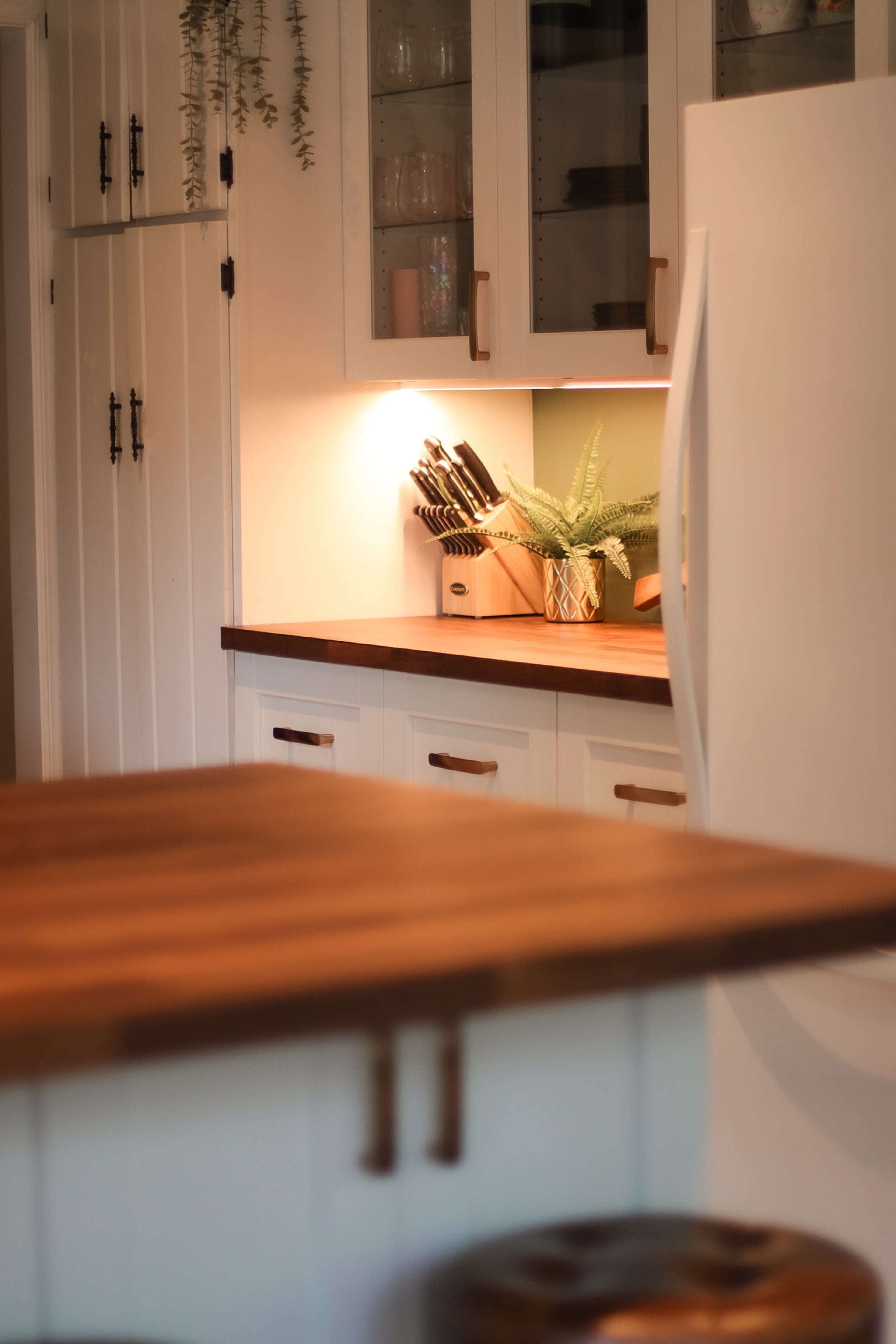 A clean kitchen features wooden countertops, white cabinets, and a well-organized knife rack illuminated by soft lighting.