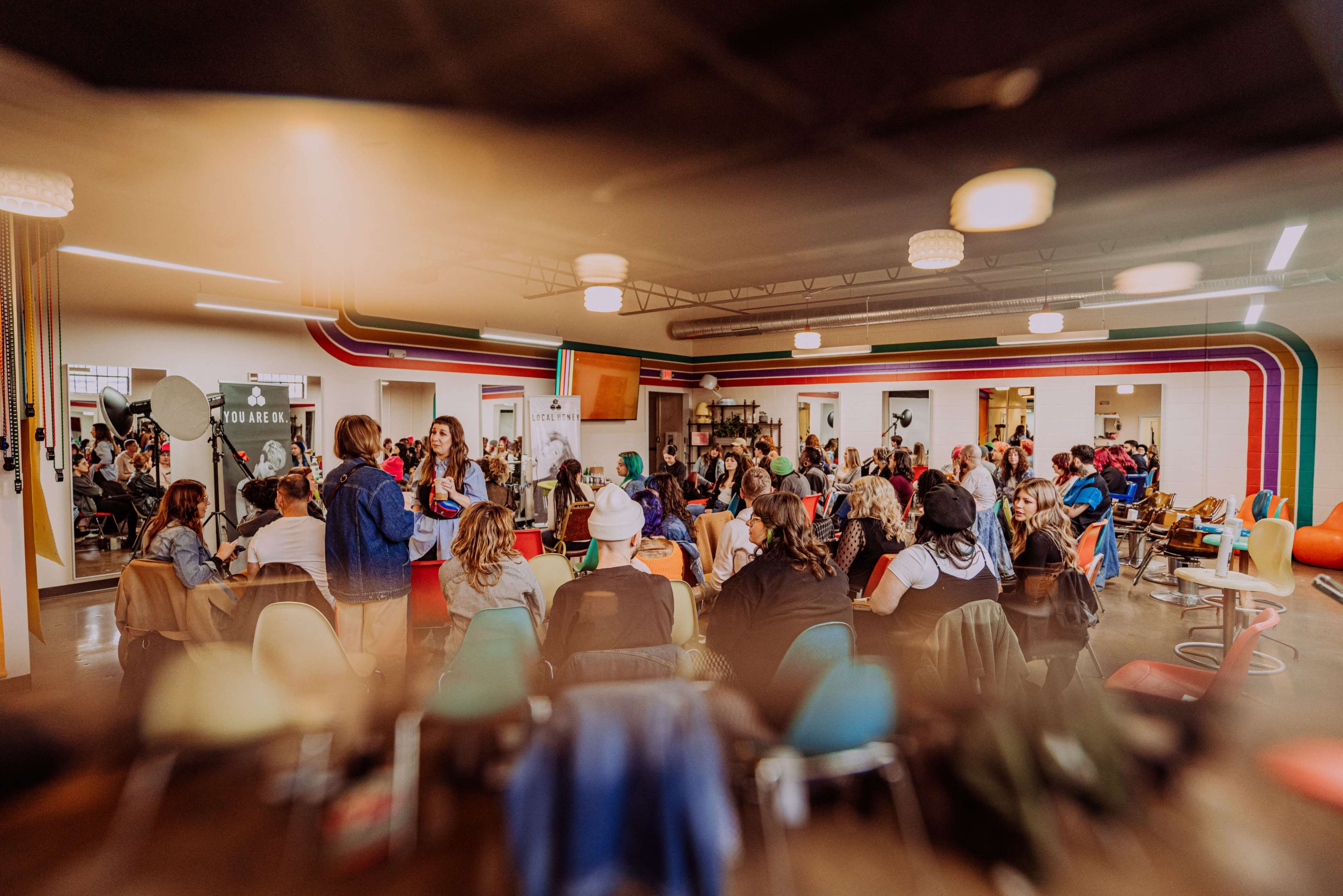 A large group of people is seated in a colorful community space, engaged in a discussion or presentation.