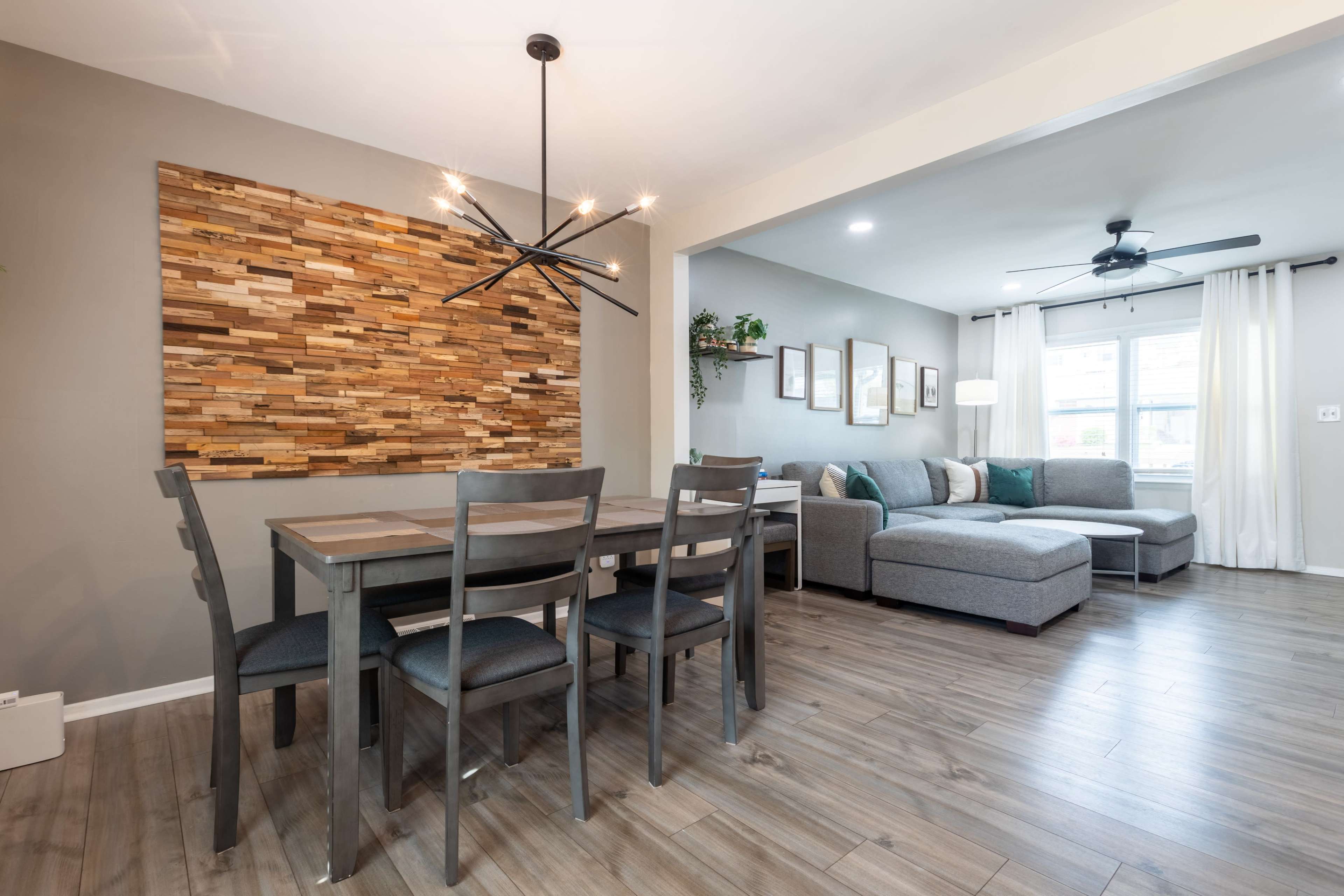 A modern dining area features a wooden table with chairs, adjacent to a living space with a sectional sofa and a decorative wall panel.