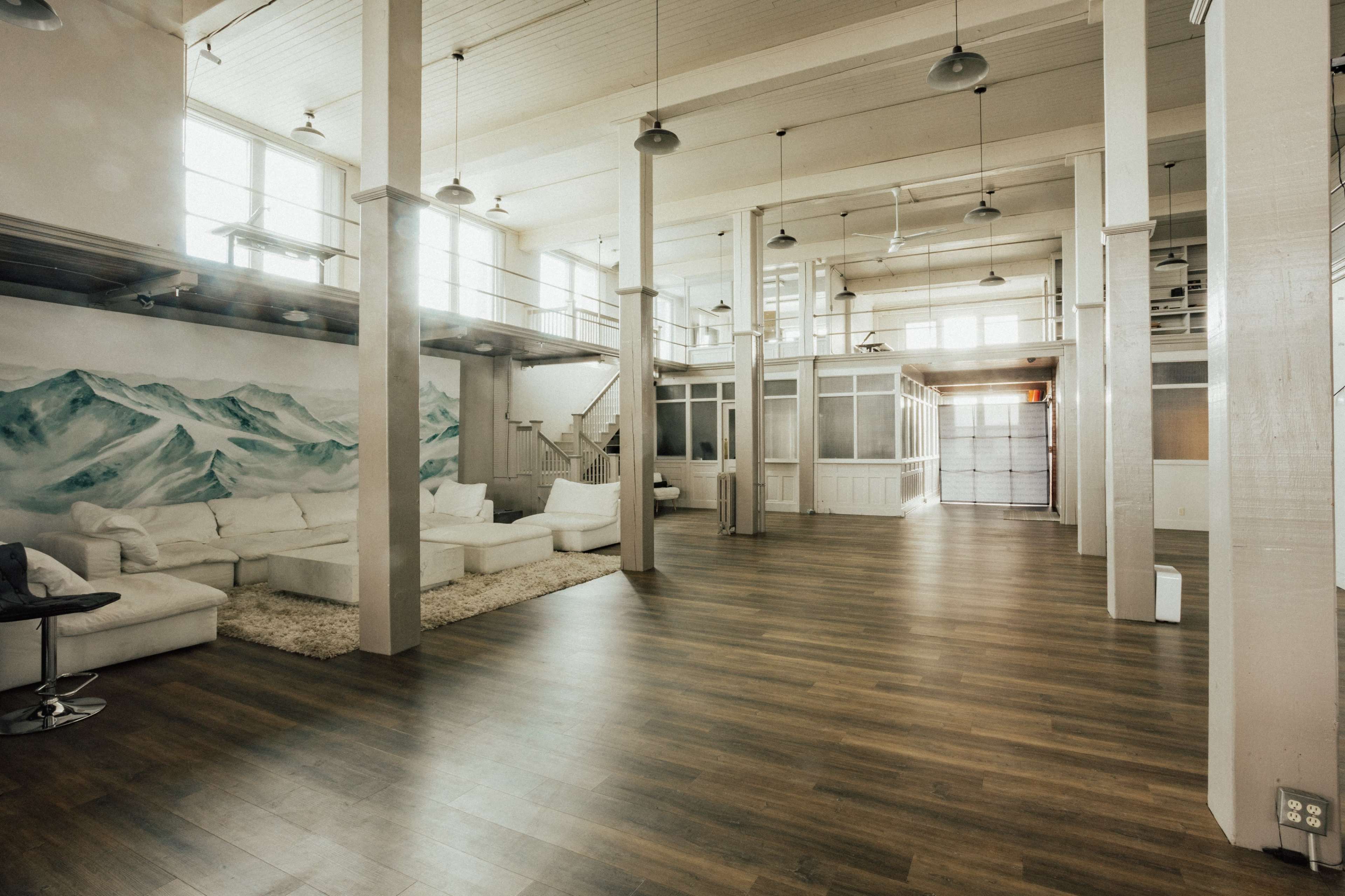 A spacious interior of a loft with wooden floors, large windows, and a mural of mountains on the wall.