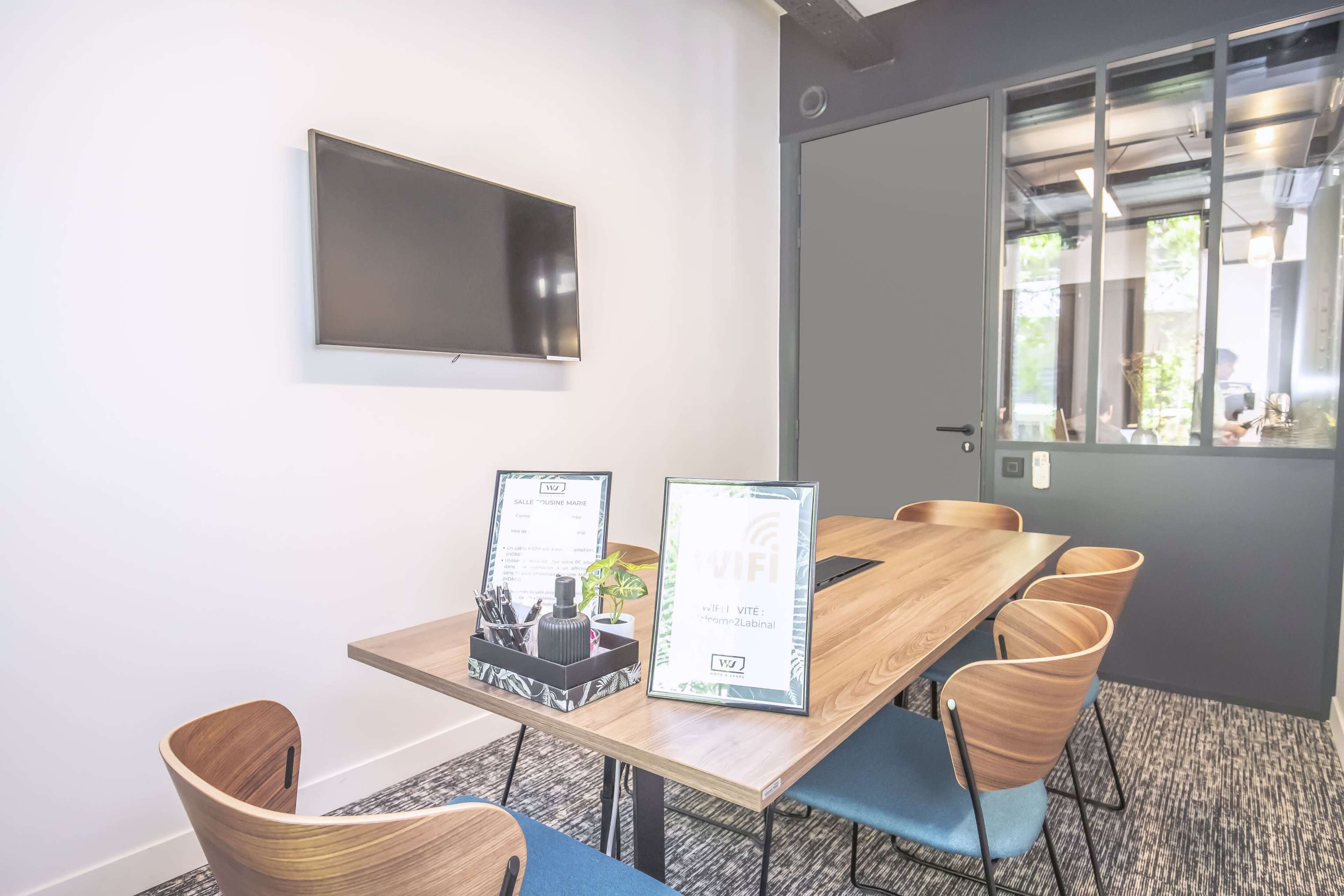 A modern conference room with a wooden table, several chairs, a television on the wall, and informational signs related to Wi-Fi.
