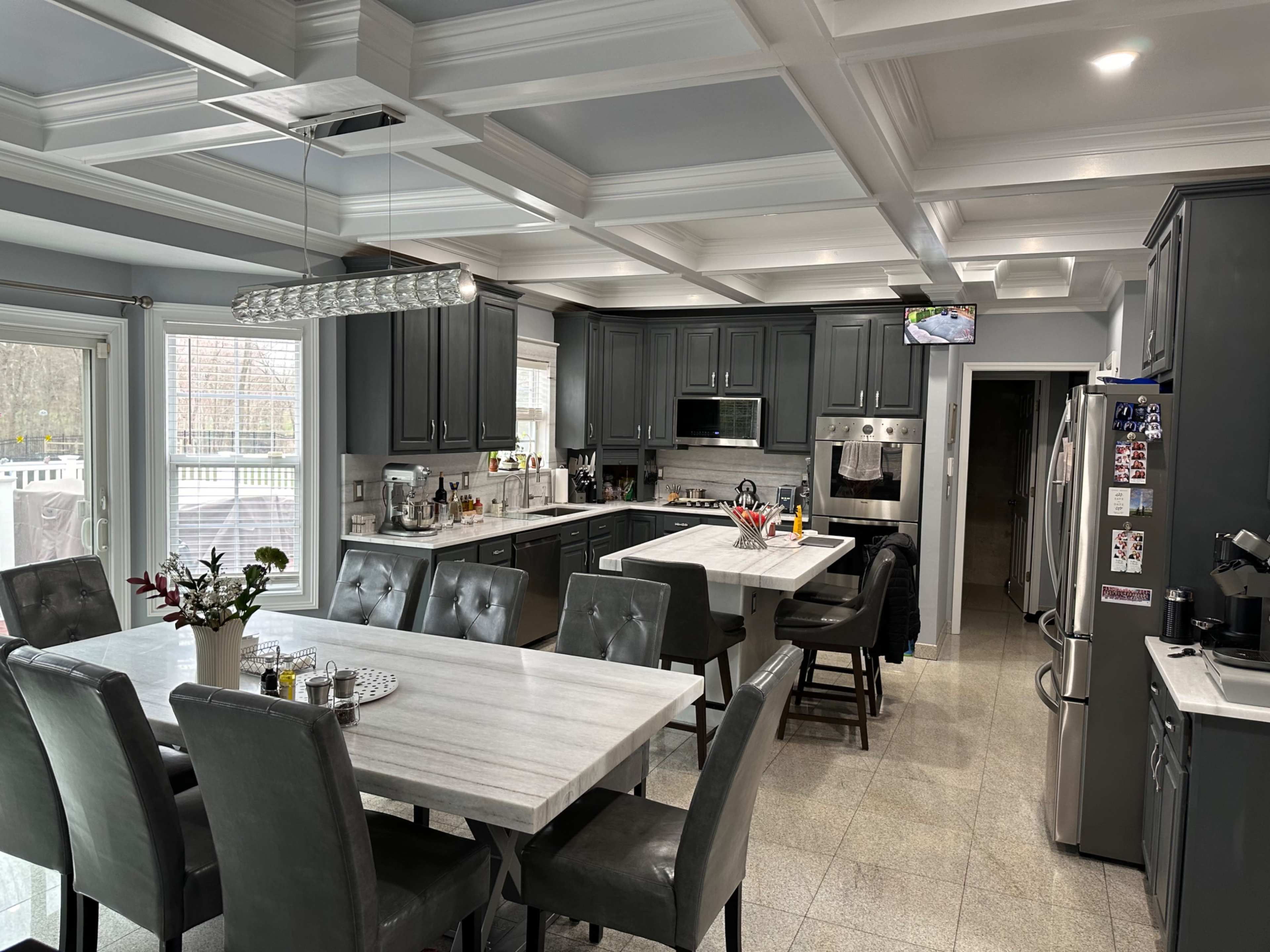 A modern kitchen with gray cabinetry, a large marble dining table, and ample natural light coming through the windows.