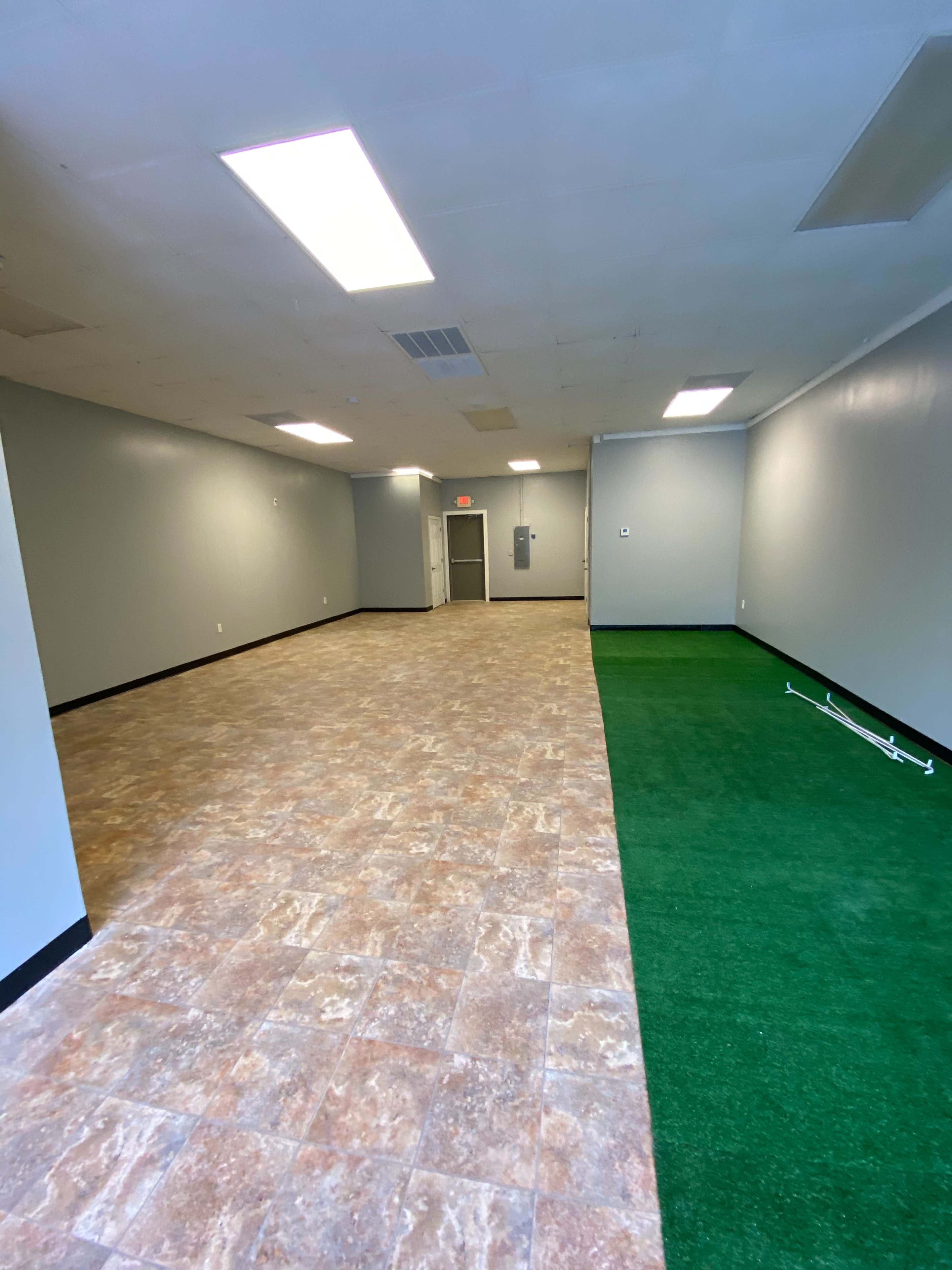 An empty indoor space with gray walls, tiled flooring, and a section of artificial grass on the right side.