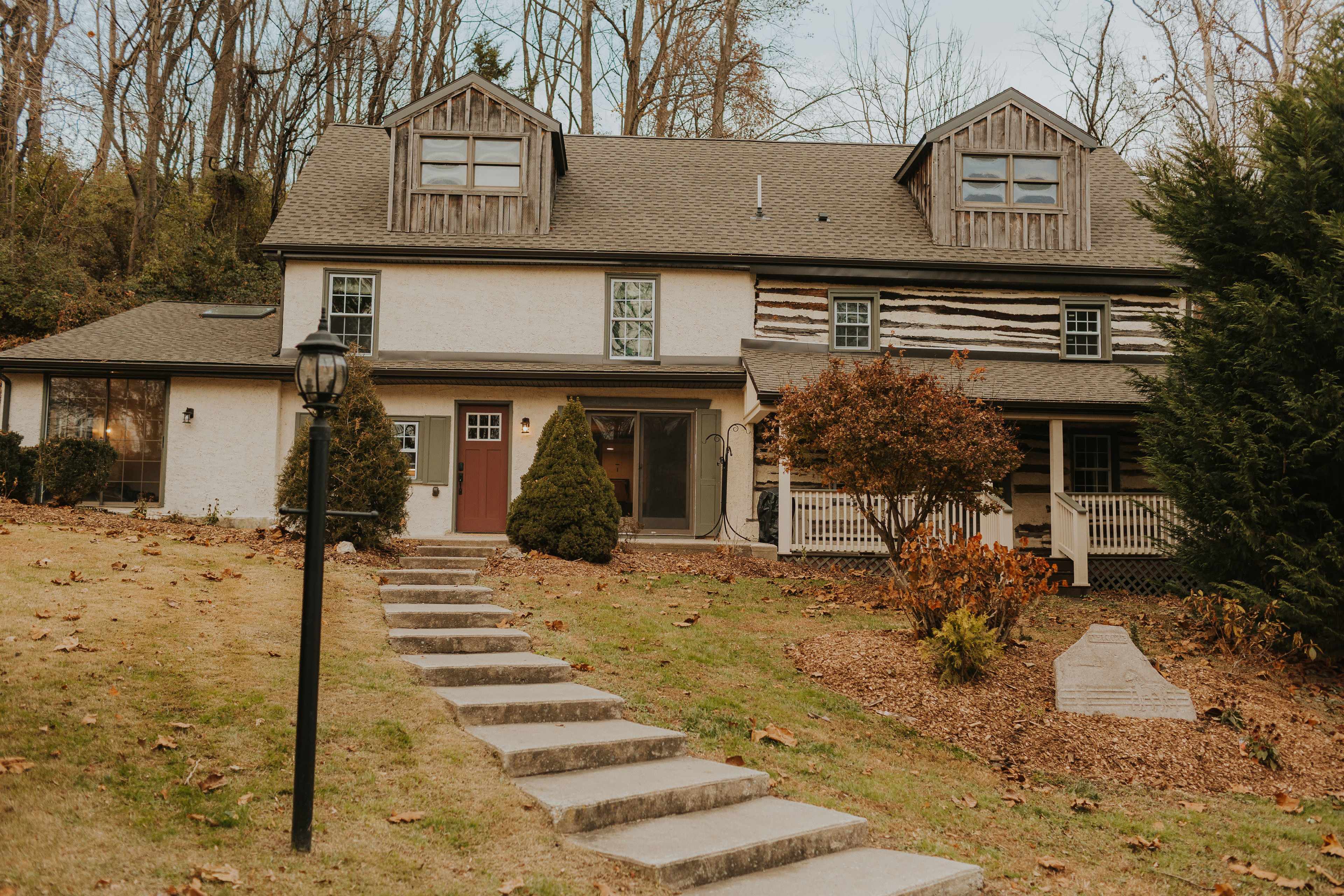 A two-story house with a combination of wooden and white exterior features a landscaped yard and a stone walkway leading to the front door.