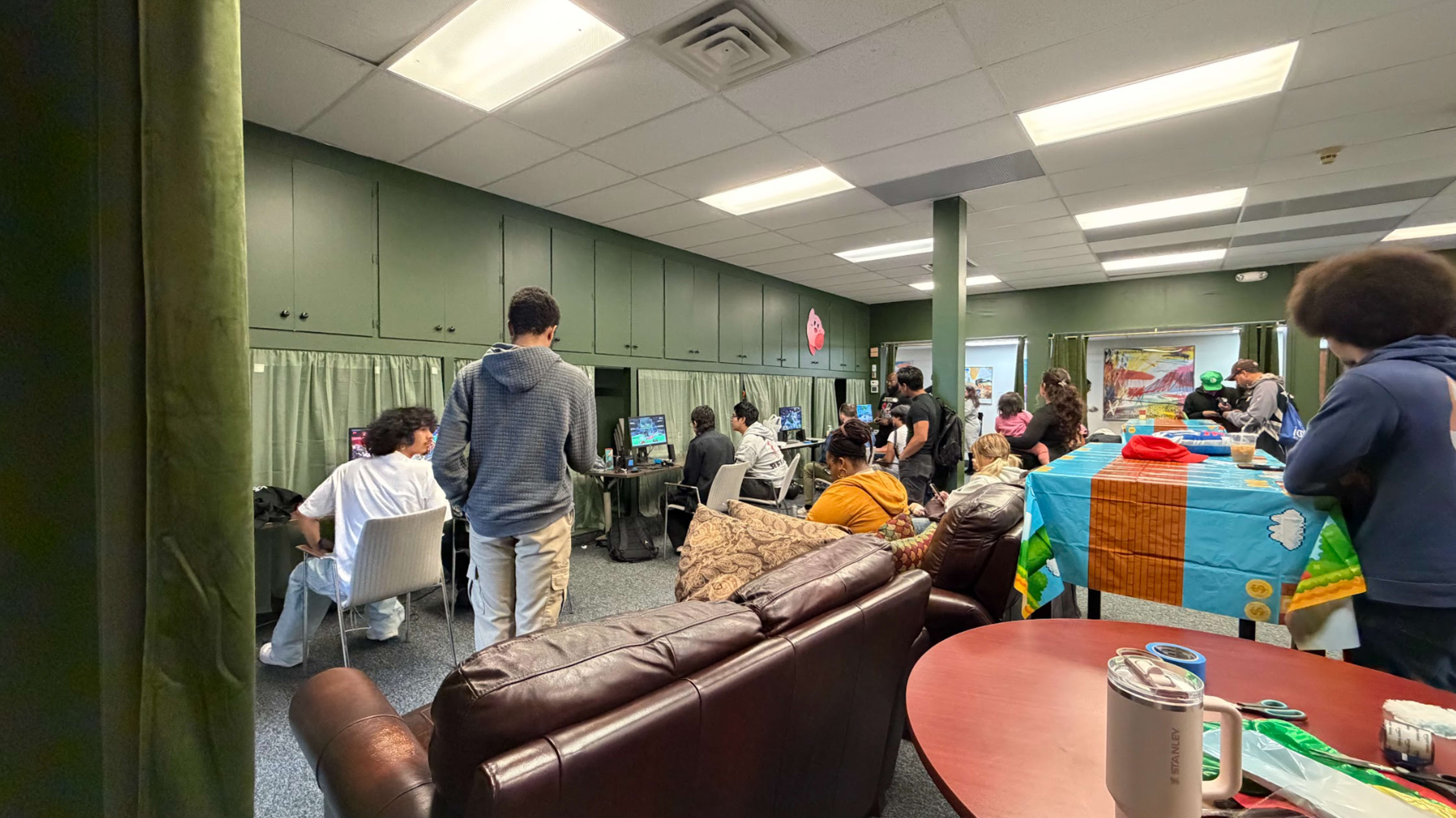 A group of people engages in gaming and socializing in a room filled with computers and tables.