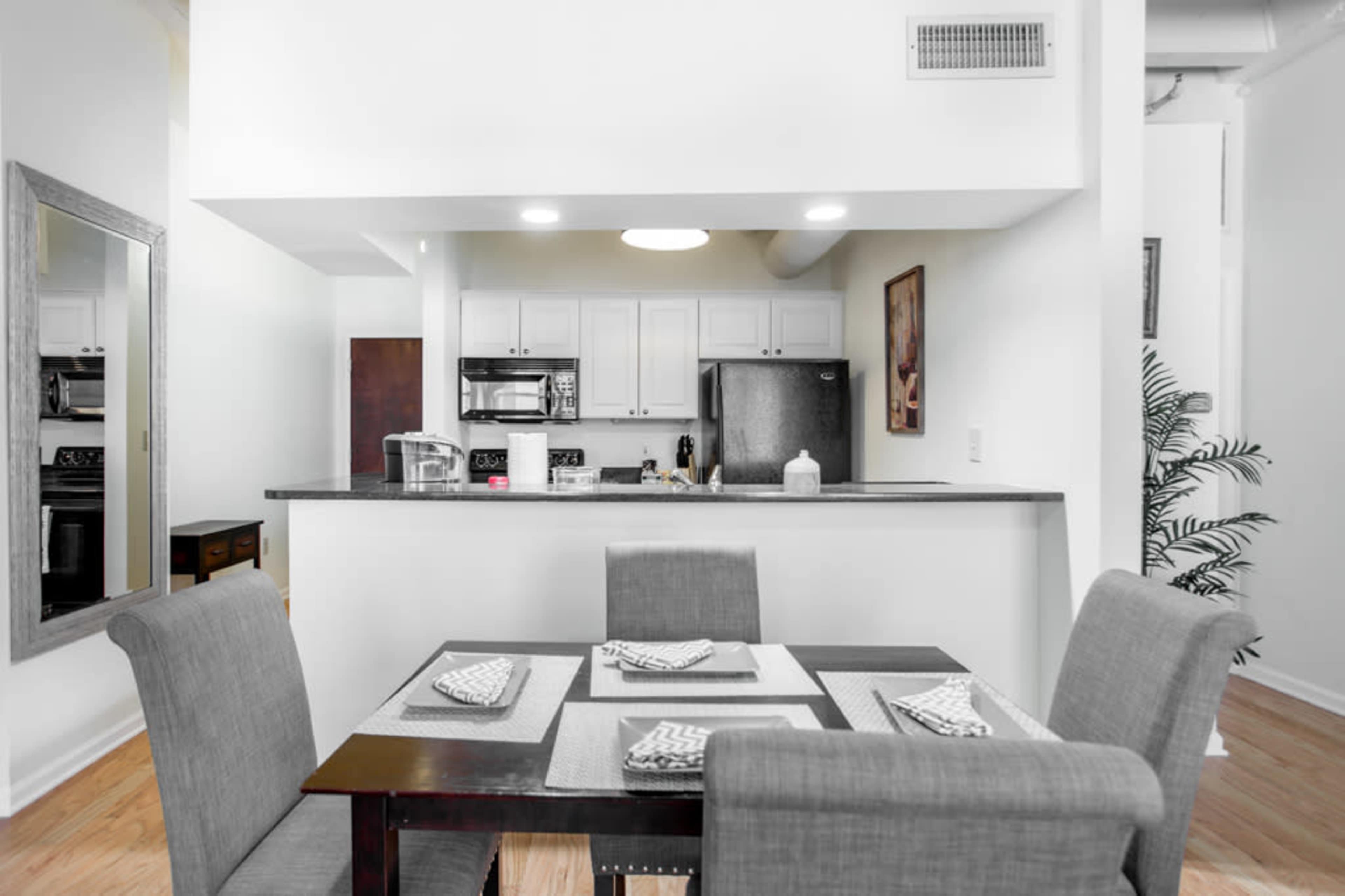 A modern dining area with a table set for four, featuring a kitchen in the background equipped with stainless steel appliances.
