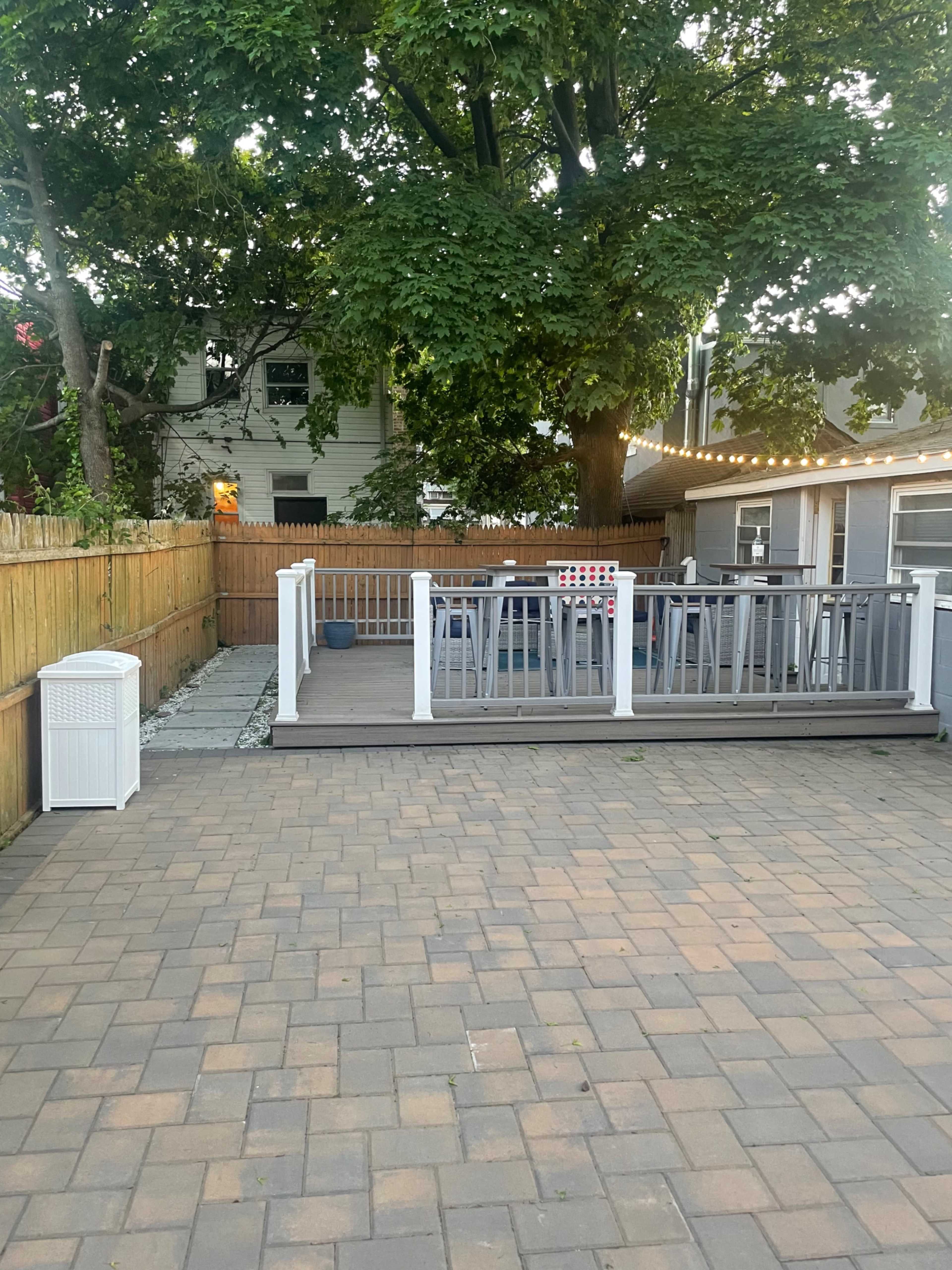 A patio area with a wooden deck featuring seating, surrounded by a fenced yard and trees.