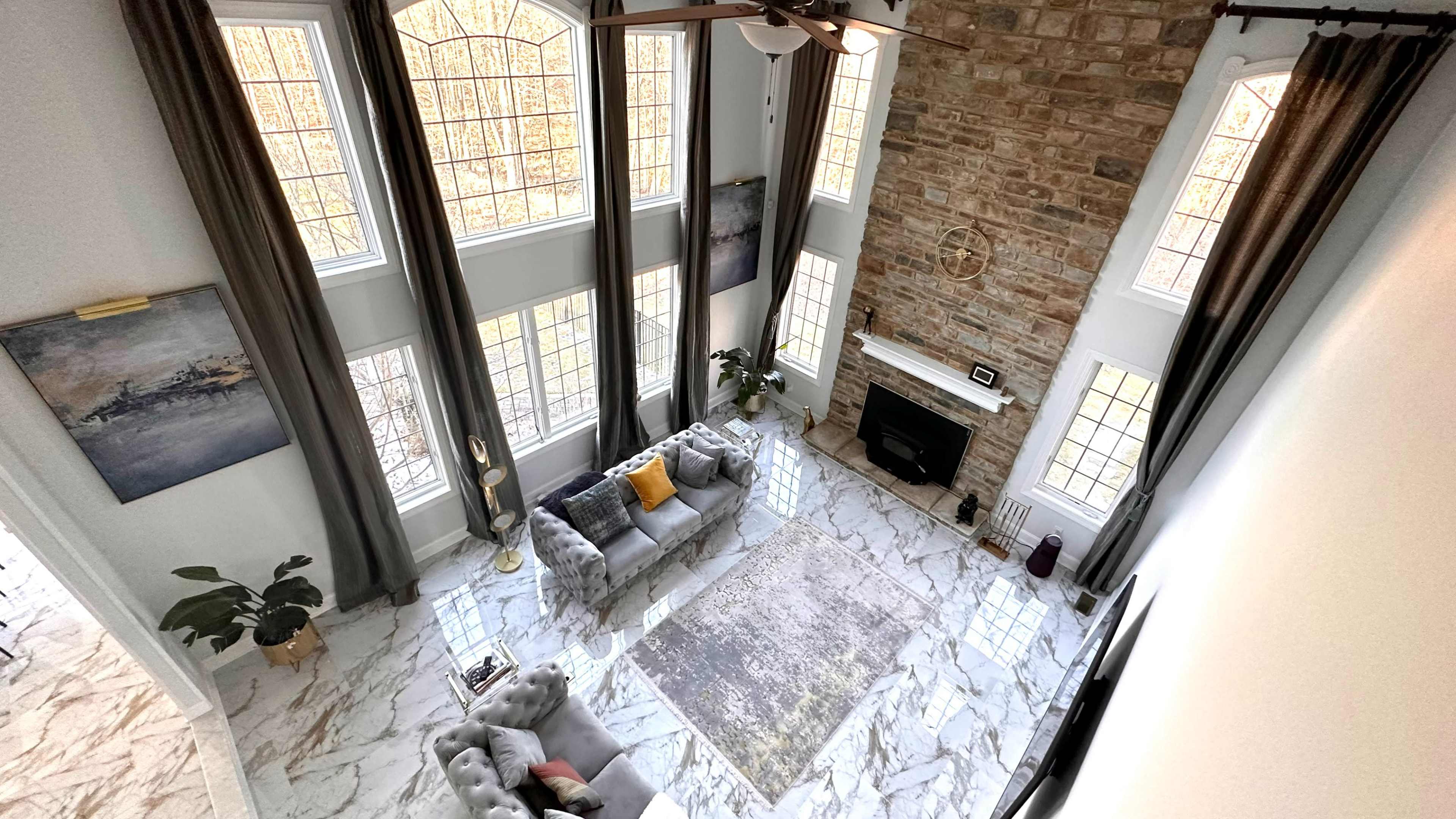 A spacious living room with large windows, stone walls, a fireplace, and elegant furniture arranged on a marble floor.