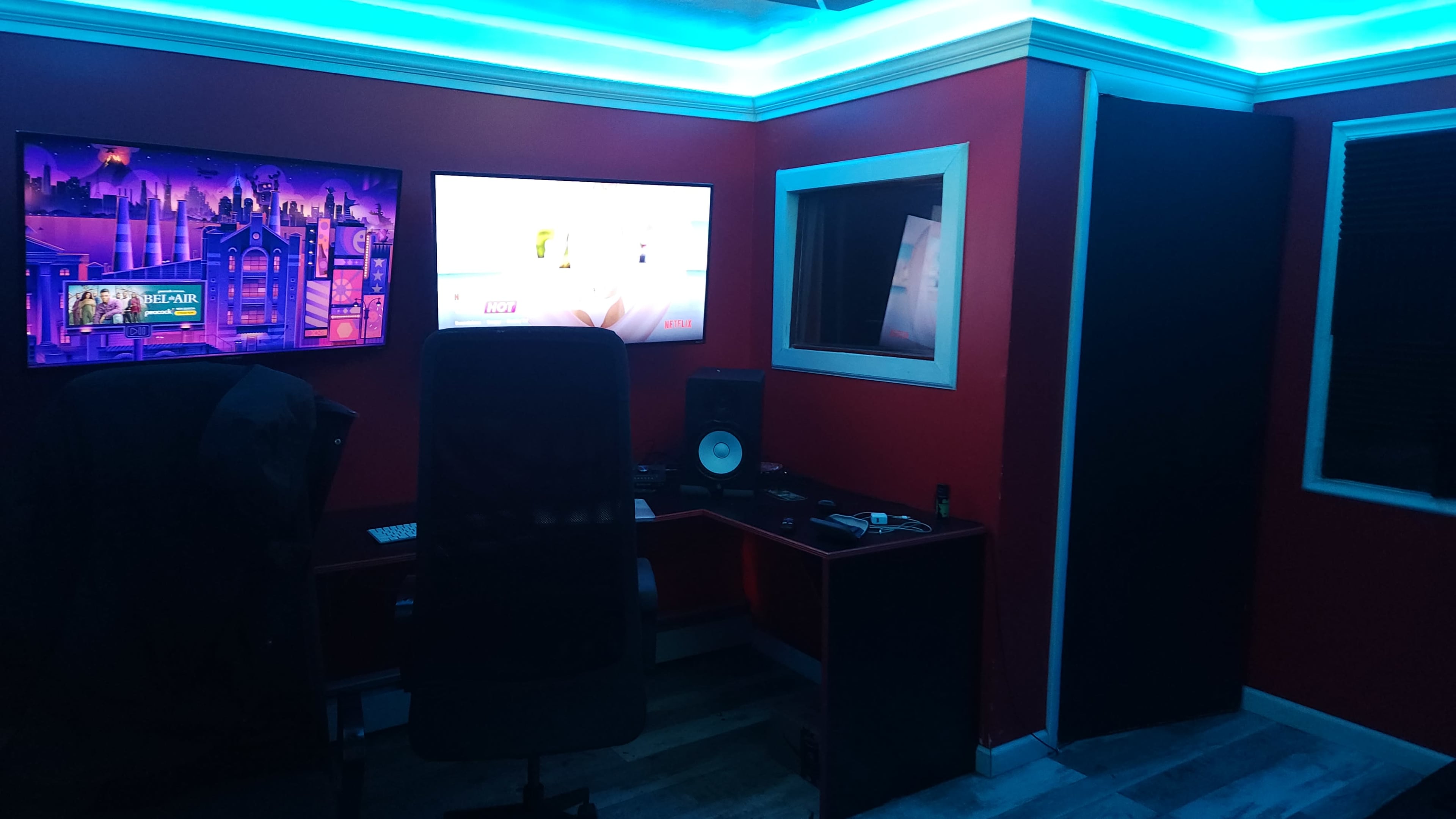 A modern recording studio with red walls, LED lighting, a large monitor, and a desk equipped with audio equipment.