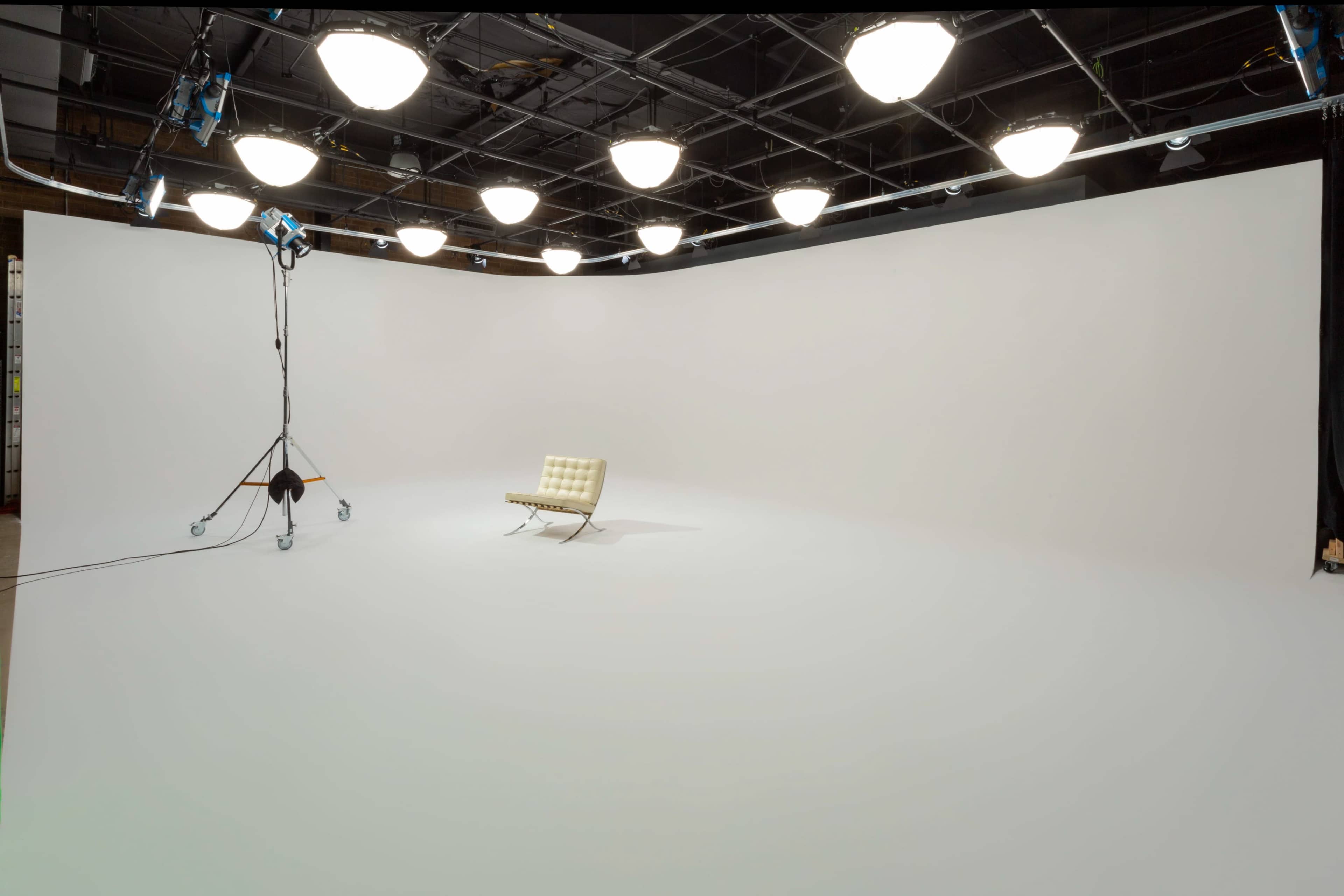 A bright, empty studio room features a single light-colored chair on a white backdrop, illuminated by overhead lights.
