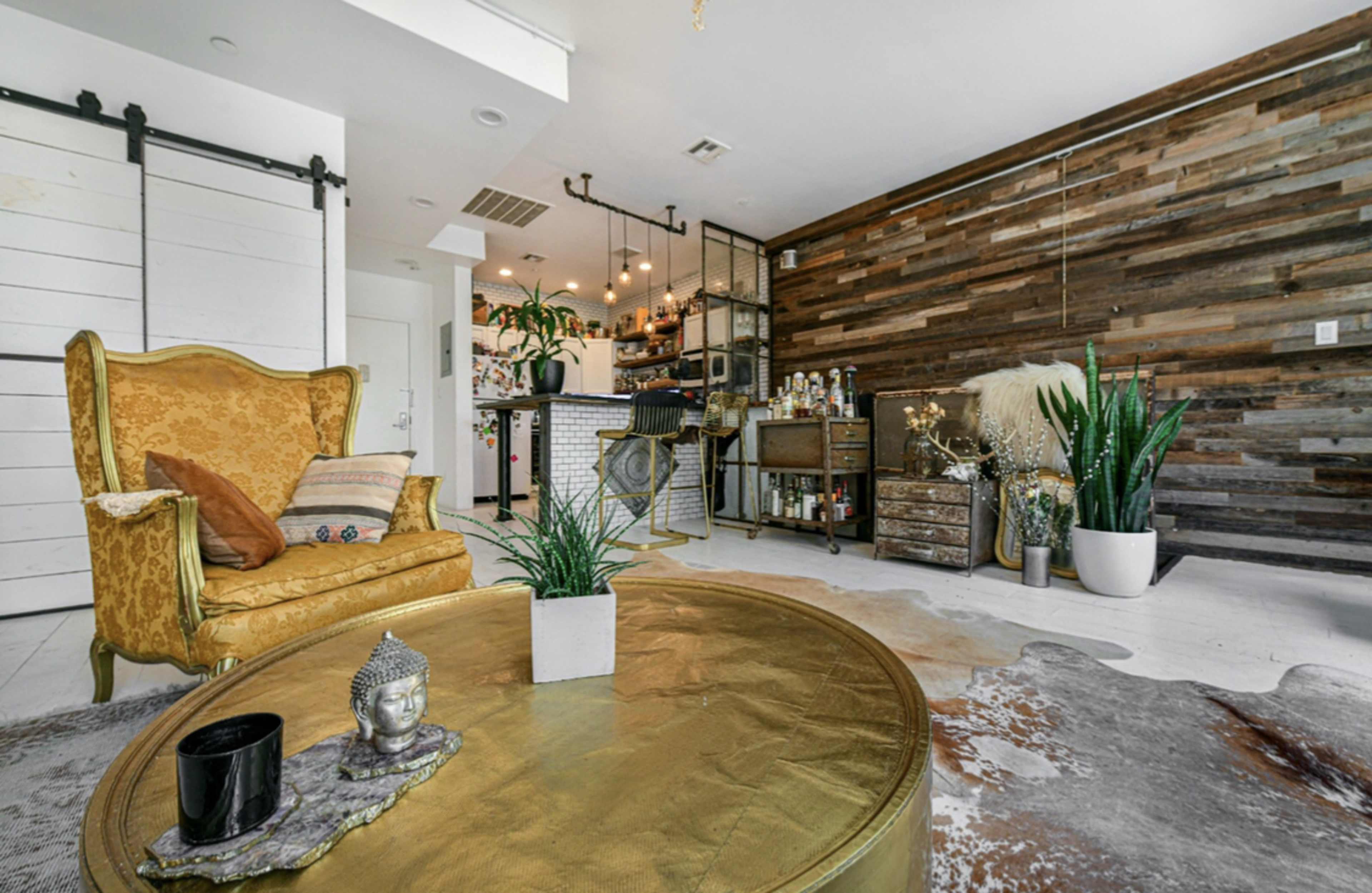 The image shows a modern living space featuring a vintage gold armchair, a round coffee table, and a decorative wall made of wooden planks.