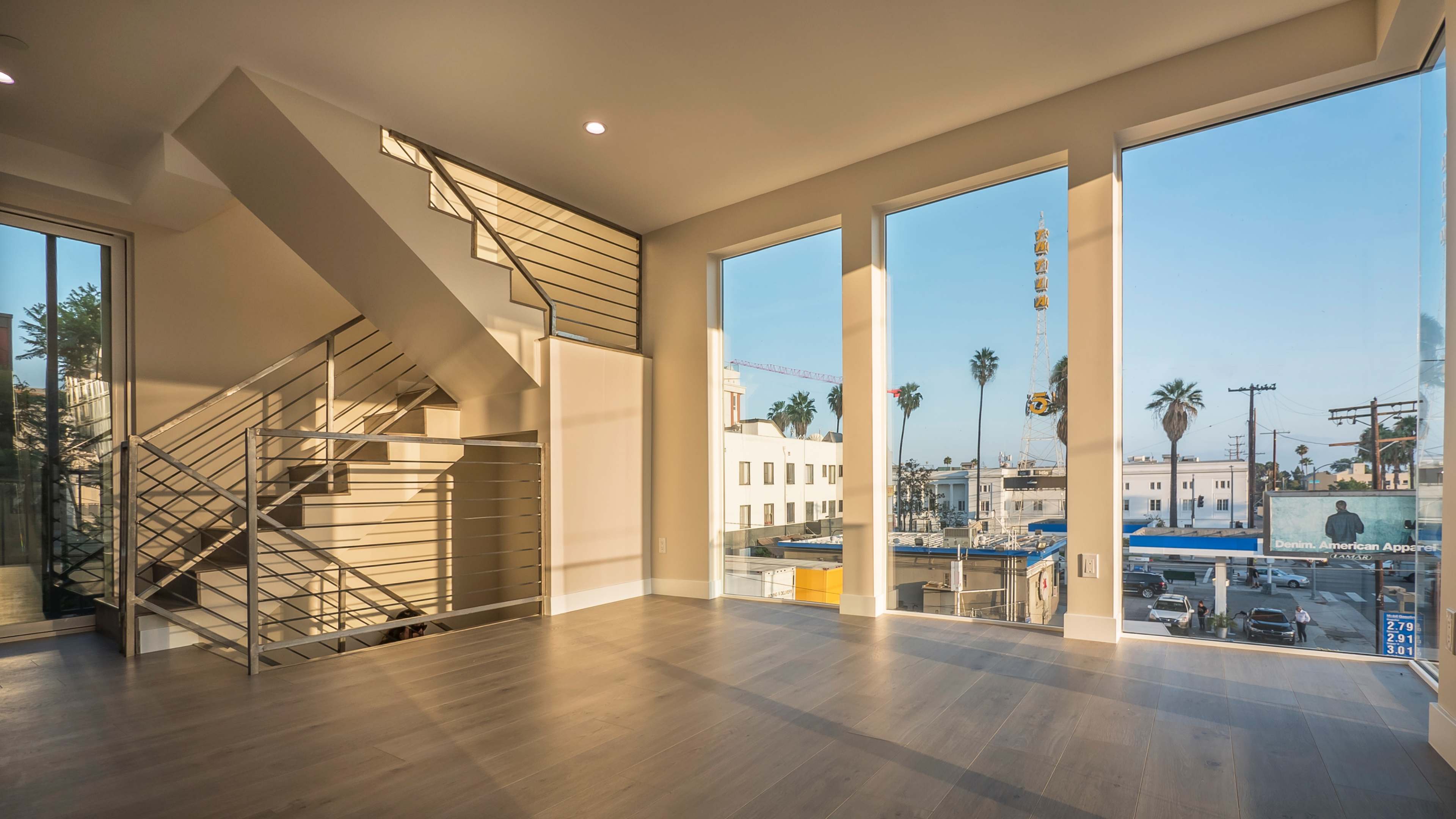 A modern, open-concept interior features large windows that overlook a city street with palm trees and construction cranes.