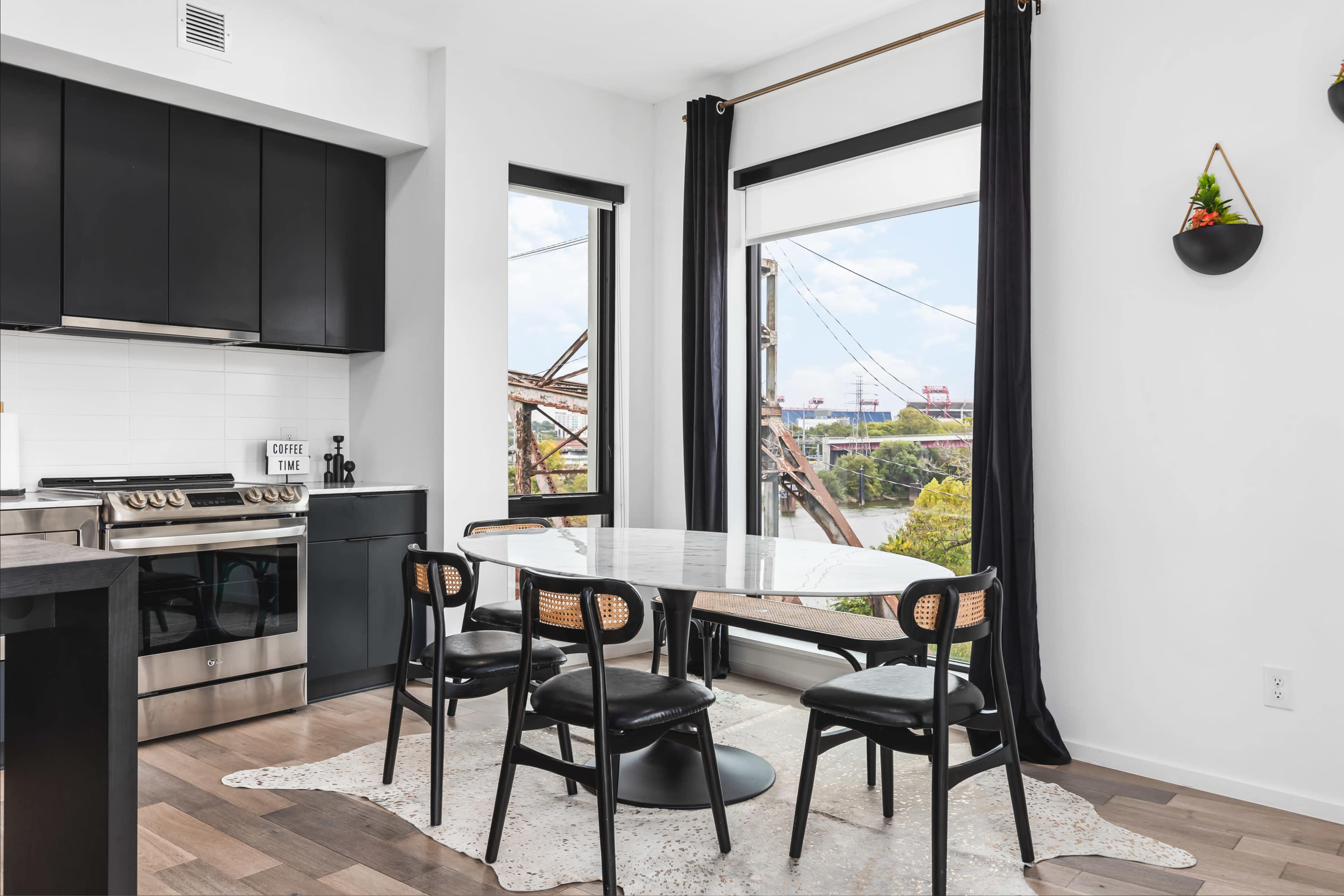 A modern kitchen with black cabinets, a marble dining table, and views of a bridge through large windows.