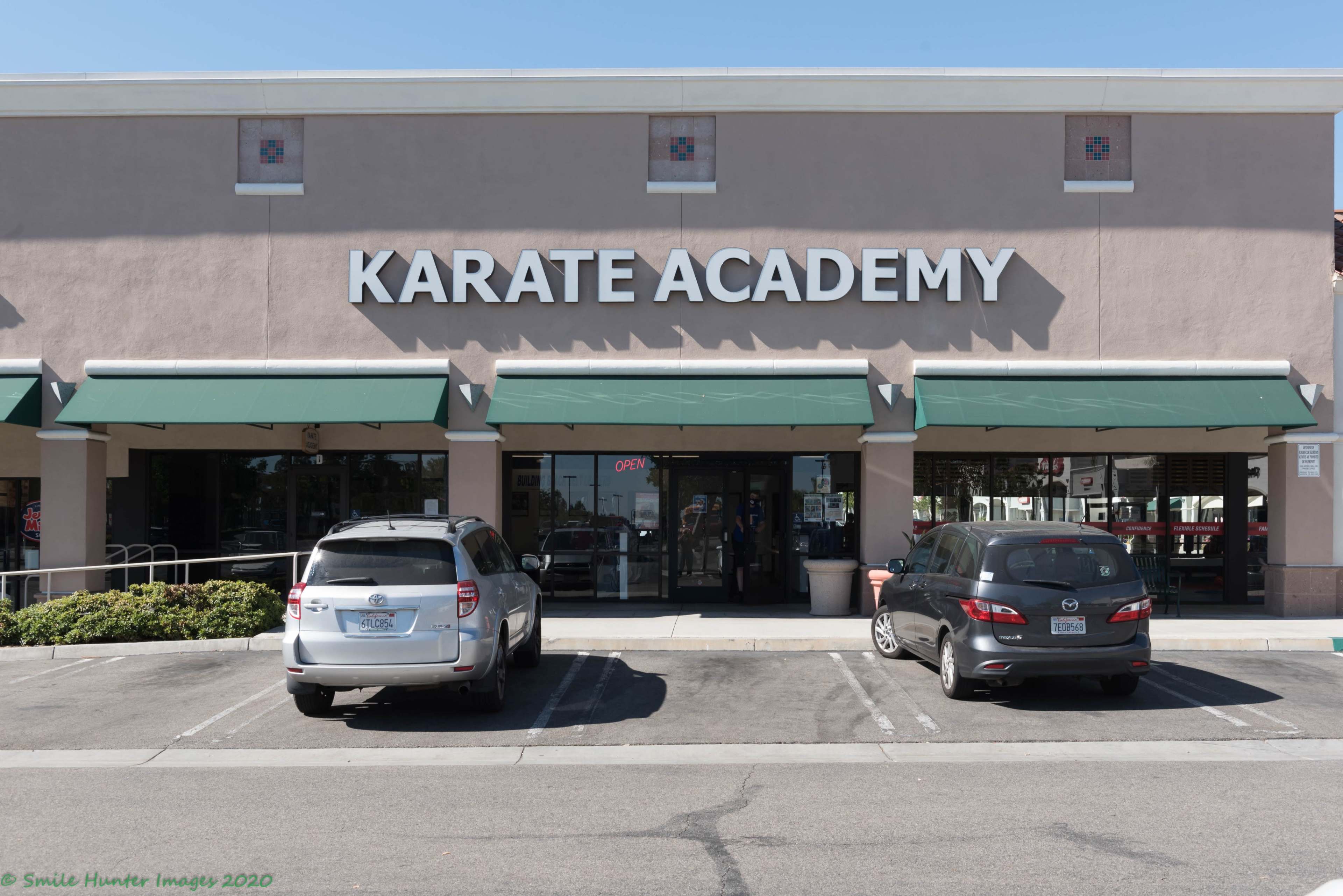 The exterior of a building labeled "Karate Academy" features a sign above the entrance, with two parked cars in the foreground.