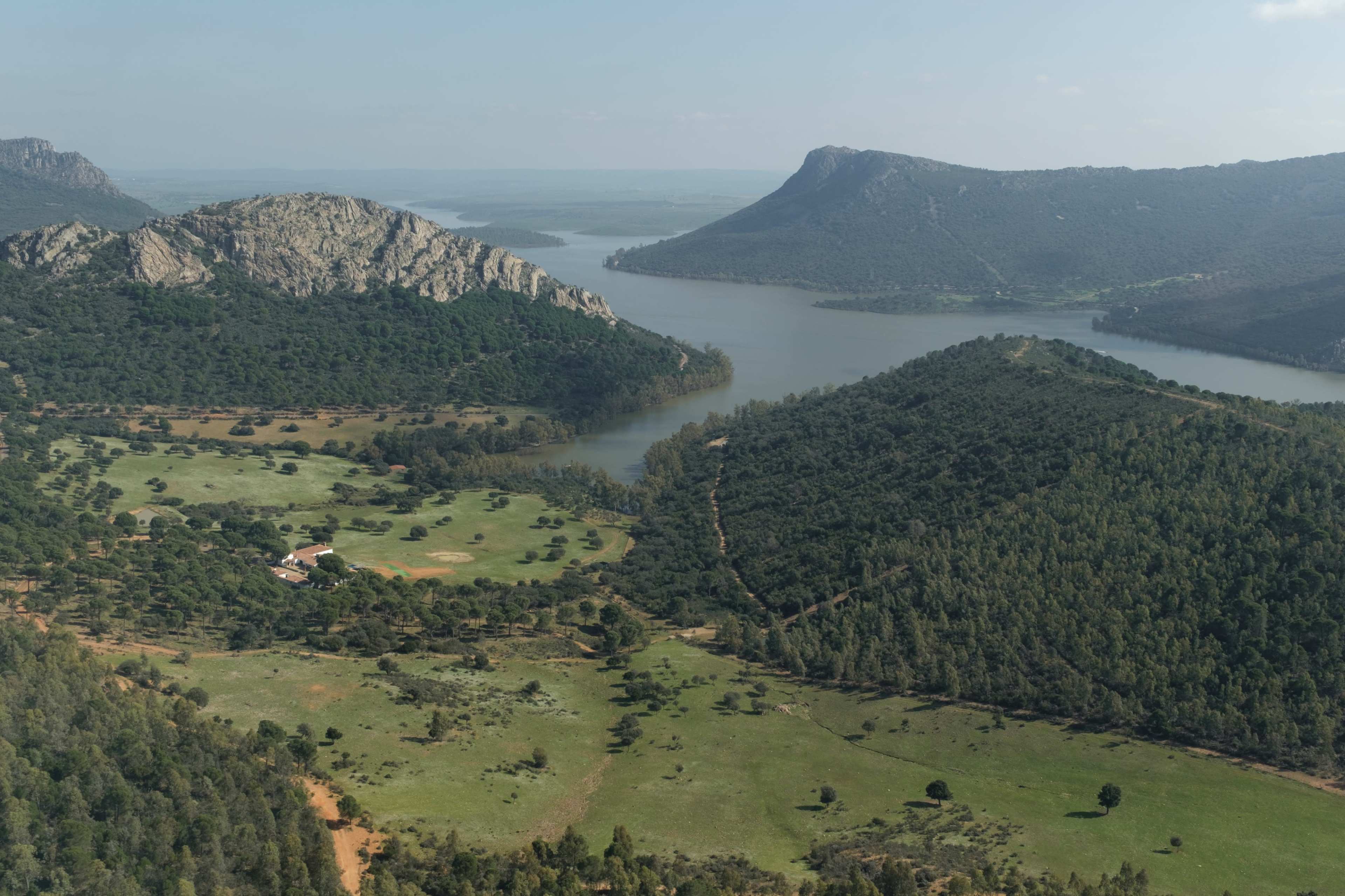 The image shows a panoramic view of a landscape featuring hills, a river, and green fields.