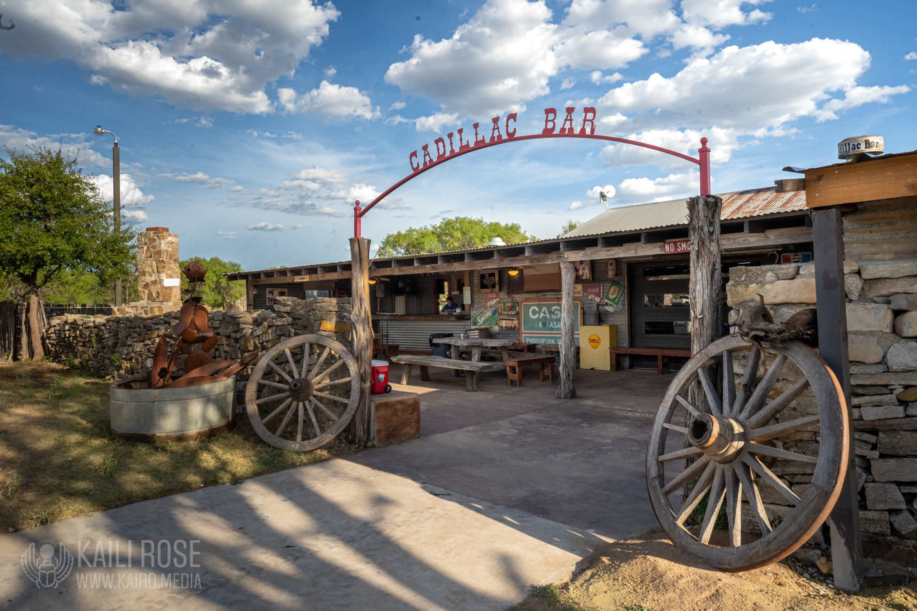 The entrance to Cadillac Bar features a rustic archway with a sign above and large wagon wheels on either side.