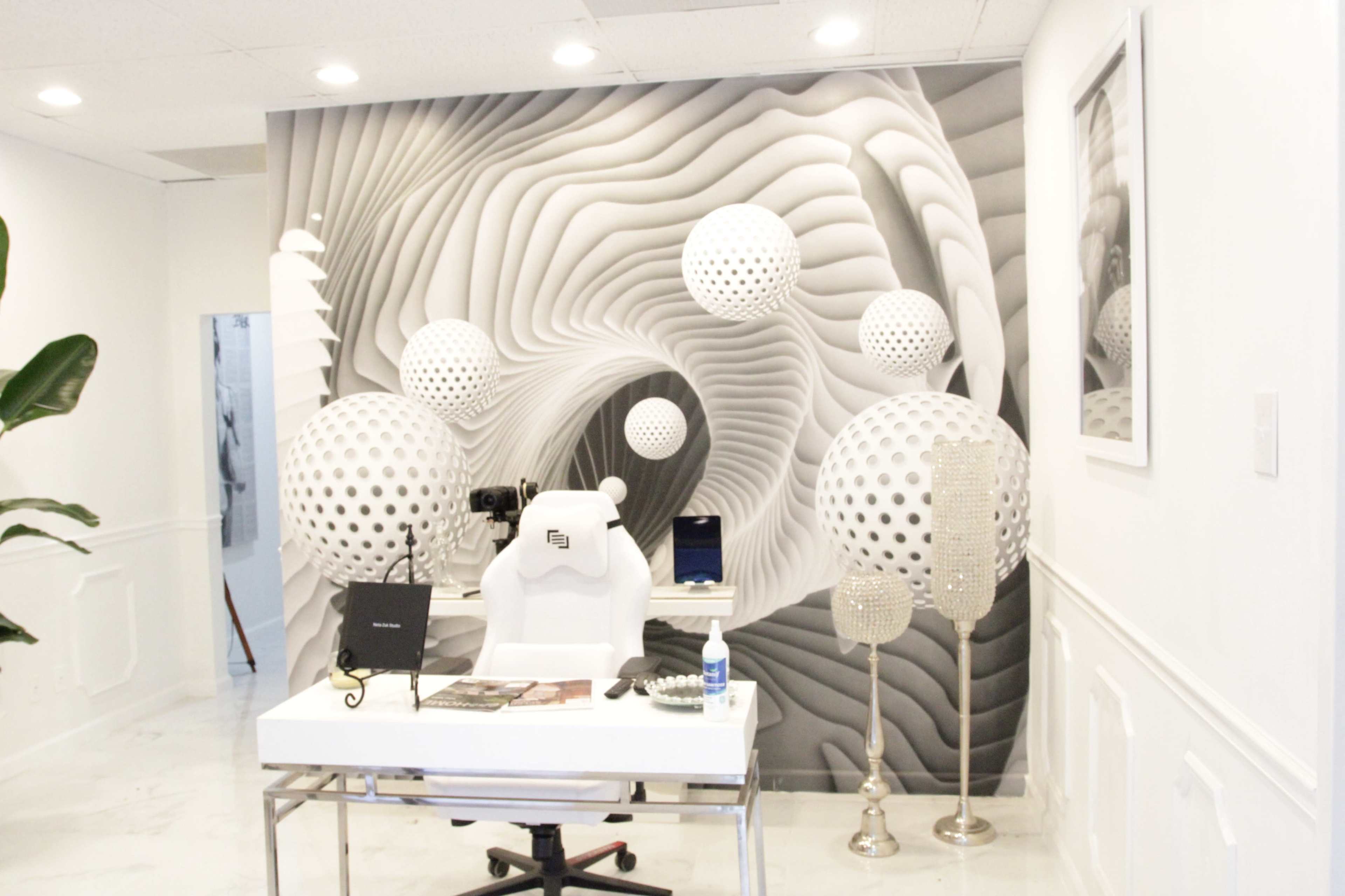 A modern office features a sleek white desk with a chair in front of a dramatic wall design of swirling patterns and three-dimensional spheres.
