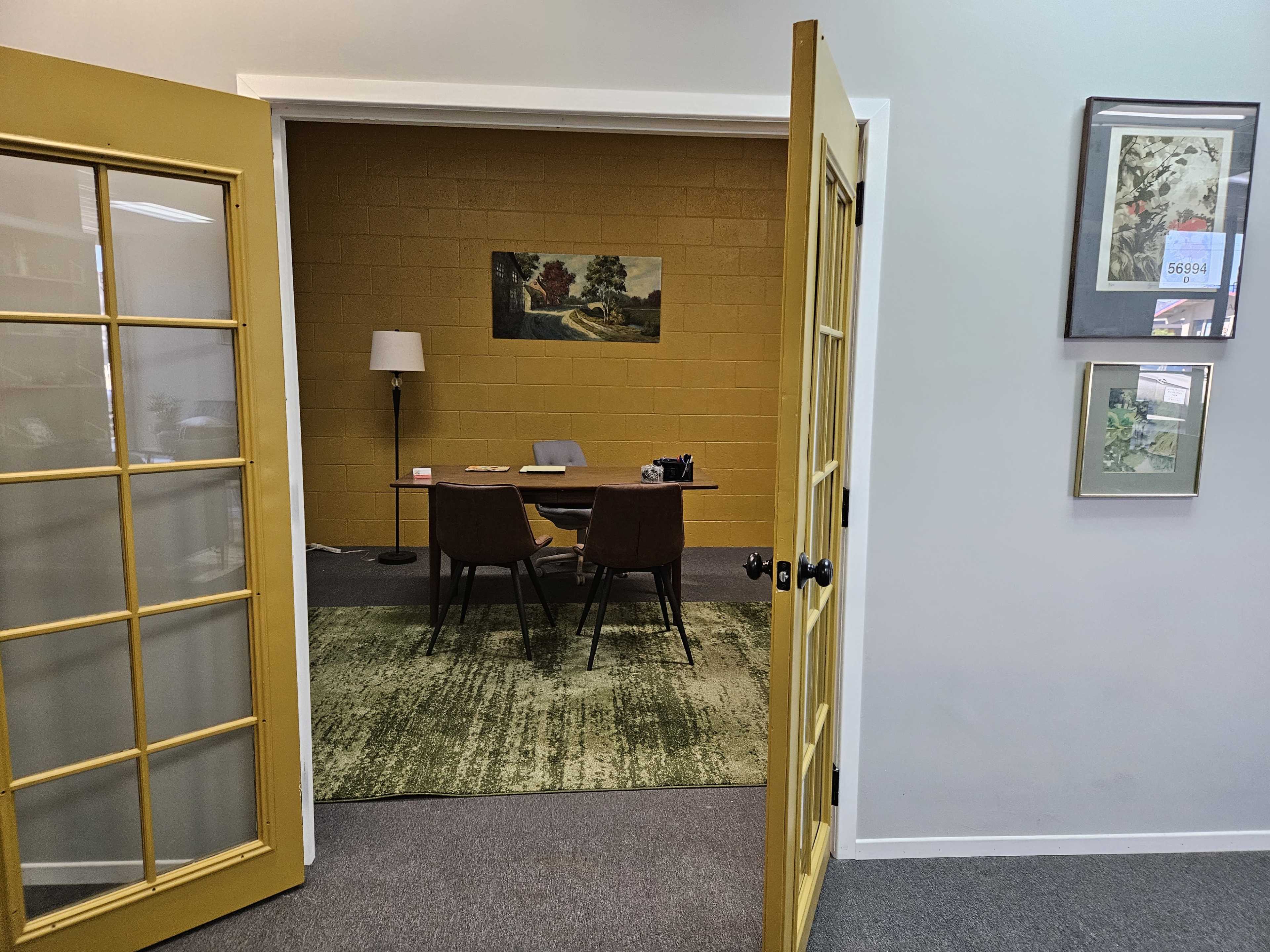 A yellow door stands open, revealing a modern office space with a table, two chairs, a lamp, and a painting on the wall.