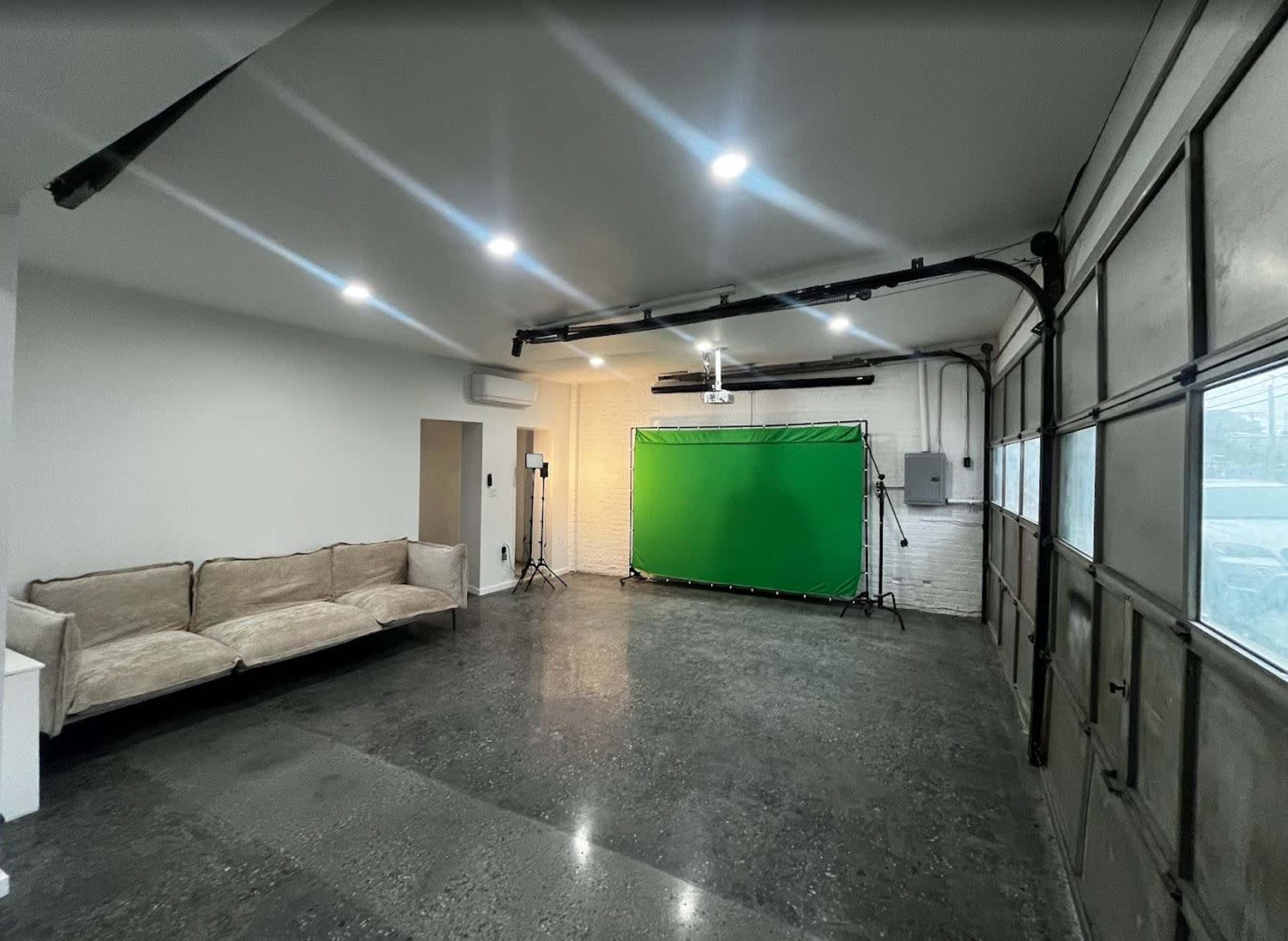 The image shows a room with a green screen setup, a beige sofa, and several lighting stands positioned around the space.