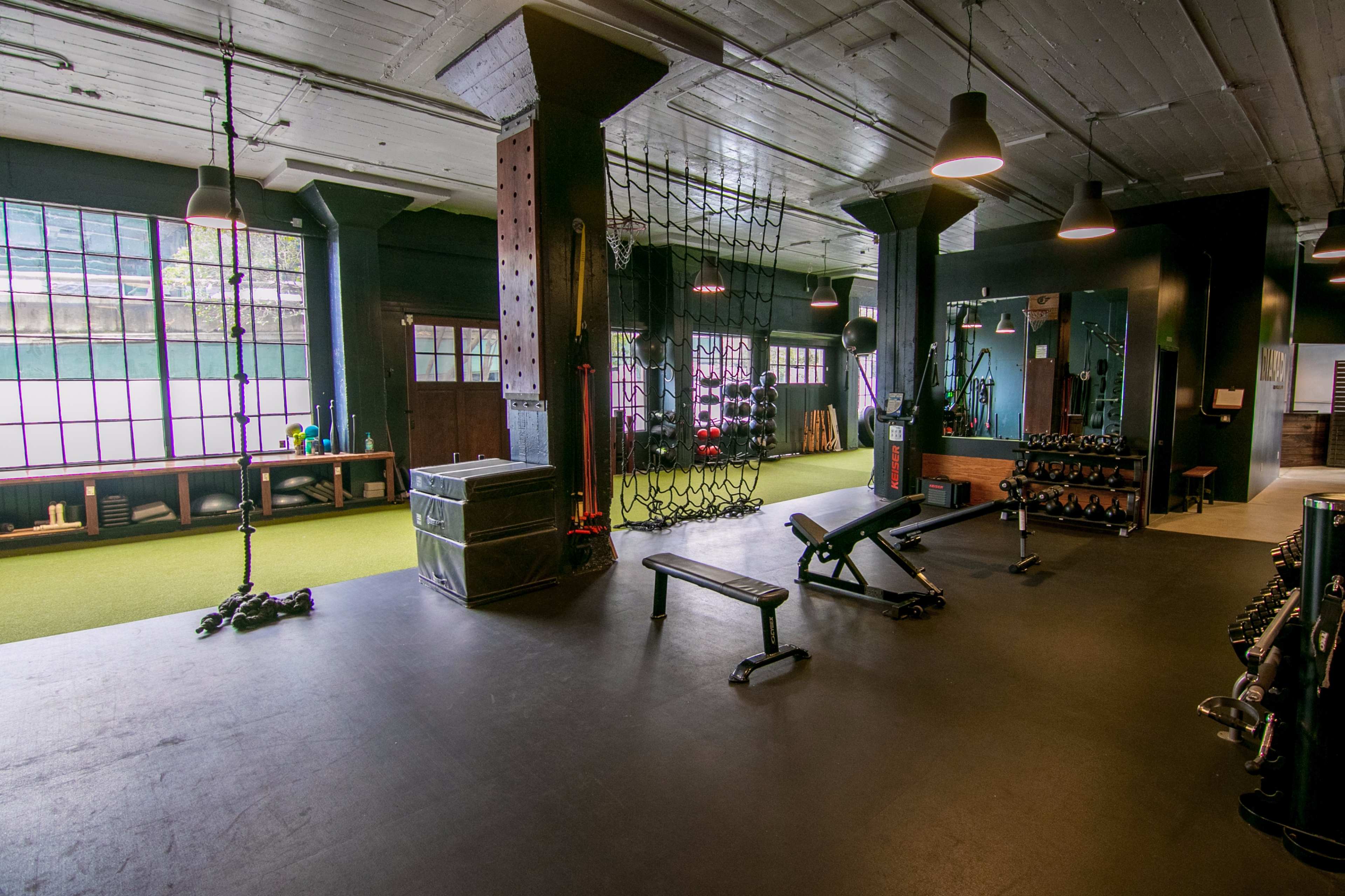 A spacious fitness gym equipped with various exercise equipment, including benches, weights, and resistance cables, along with a turf area.