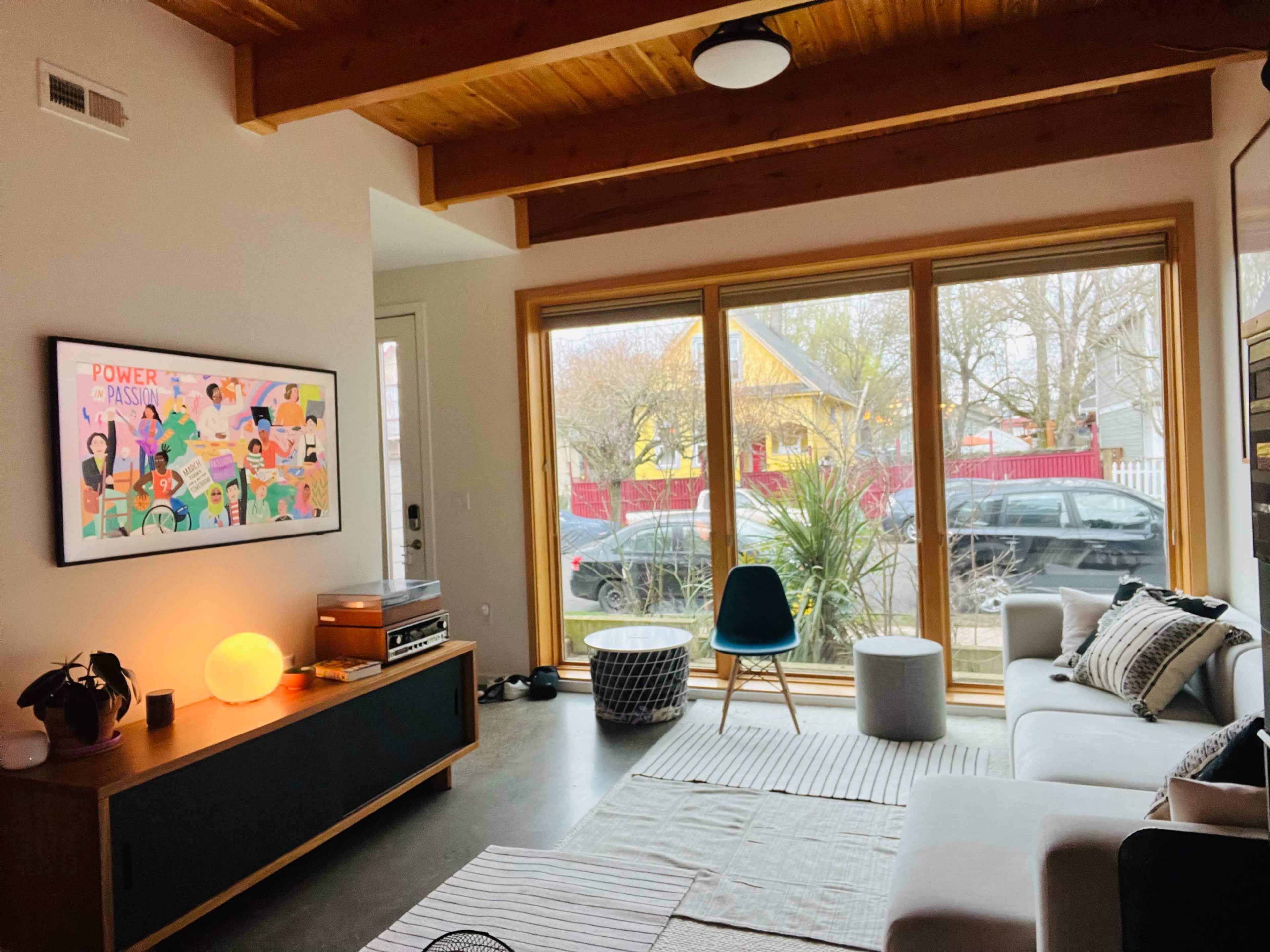 A modern living room with a large window, a sectional sofa, a coffee table, and colorful artwork on the wall.