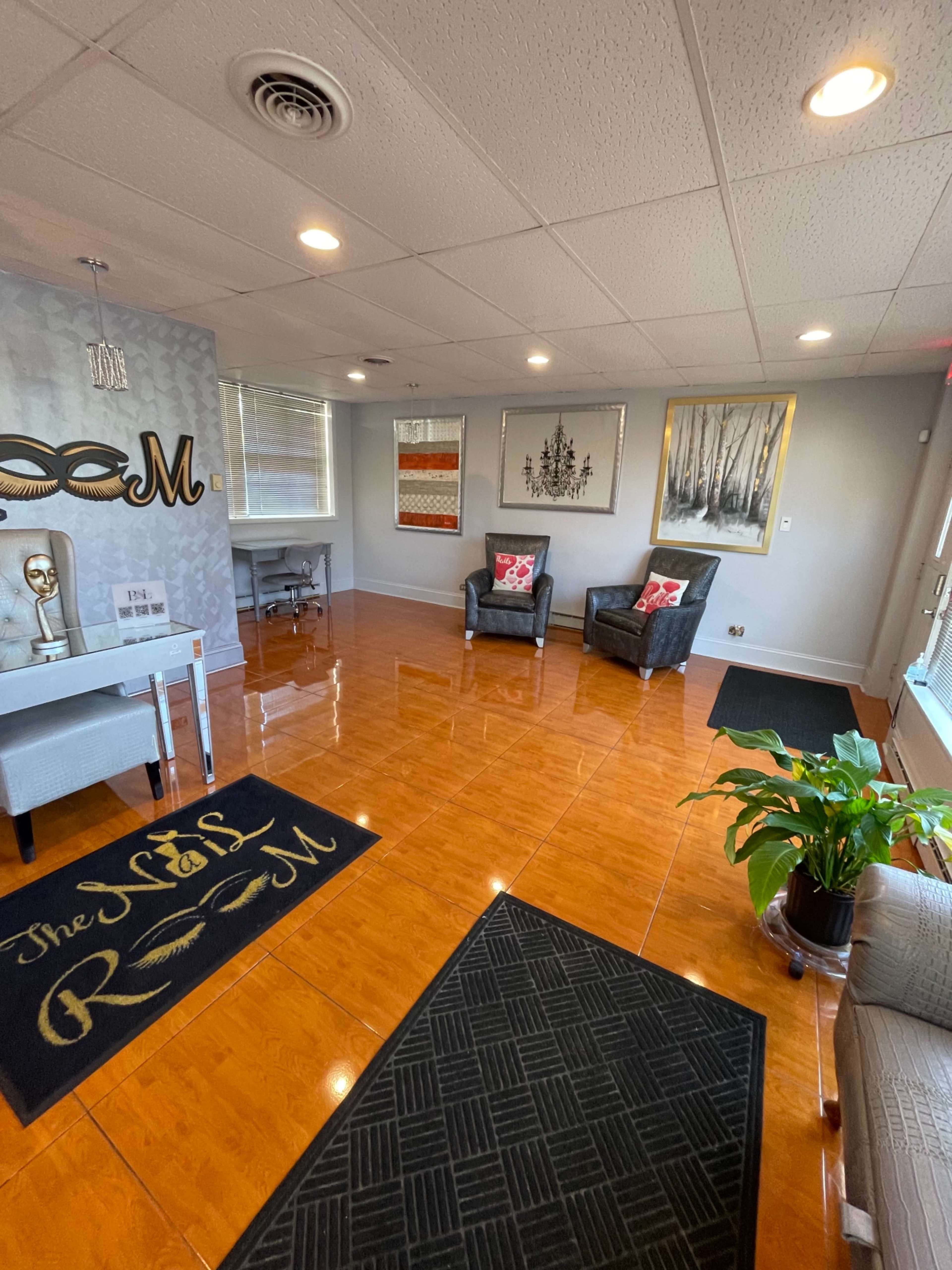 The image shows a brightly lit waiting area with polished tile floors, two armchairs, a small table, and decorative artwork on the walls.