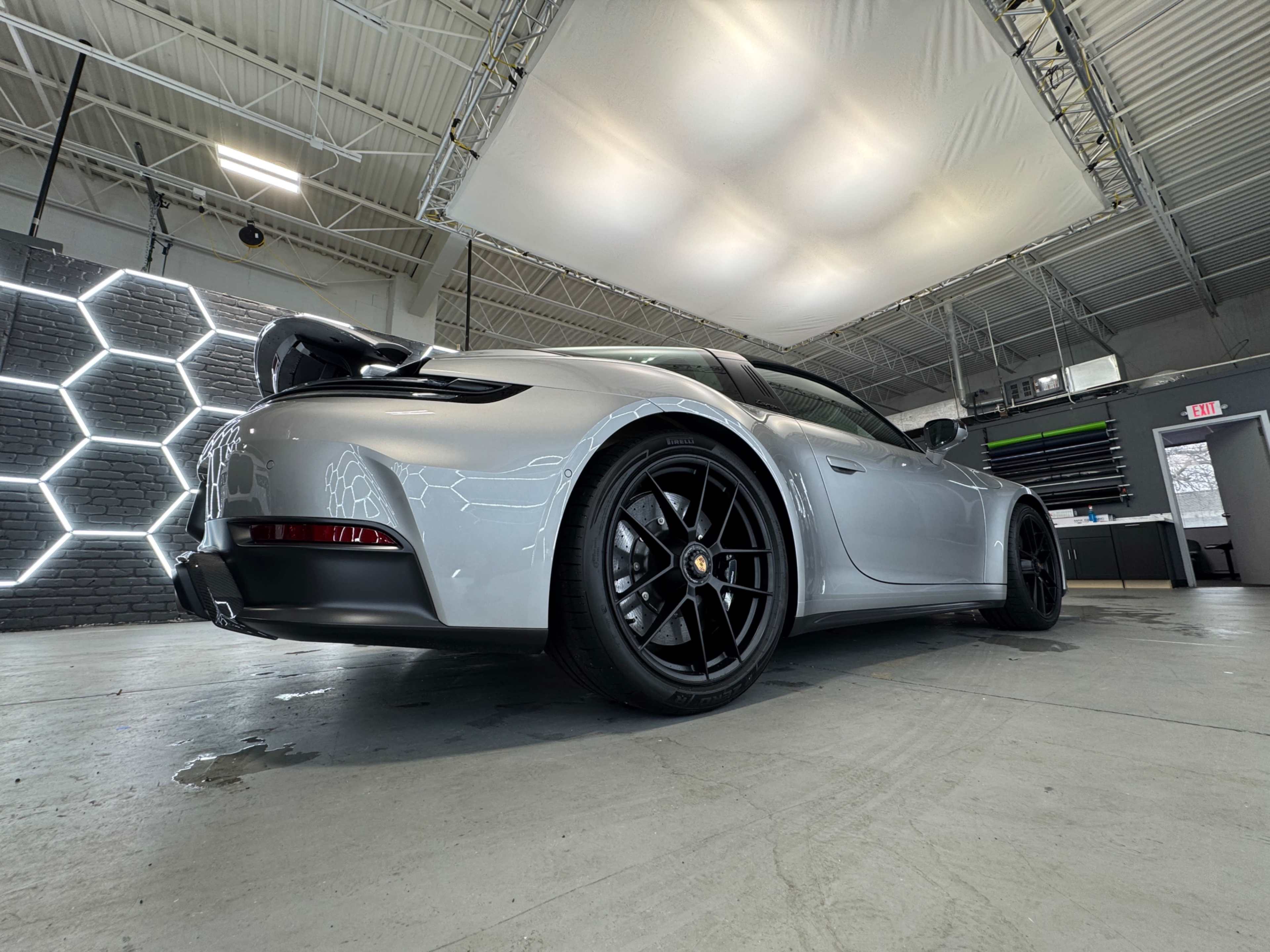 A silver sports car with a rear spoiler is parked in a well-lit showroom featuring hexagonal wall patterns.