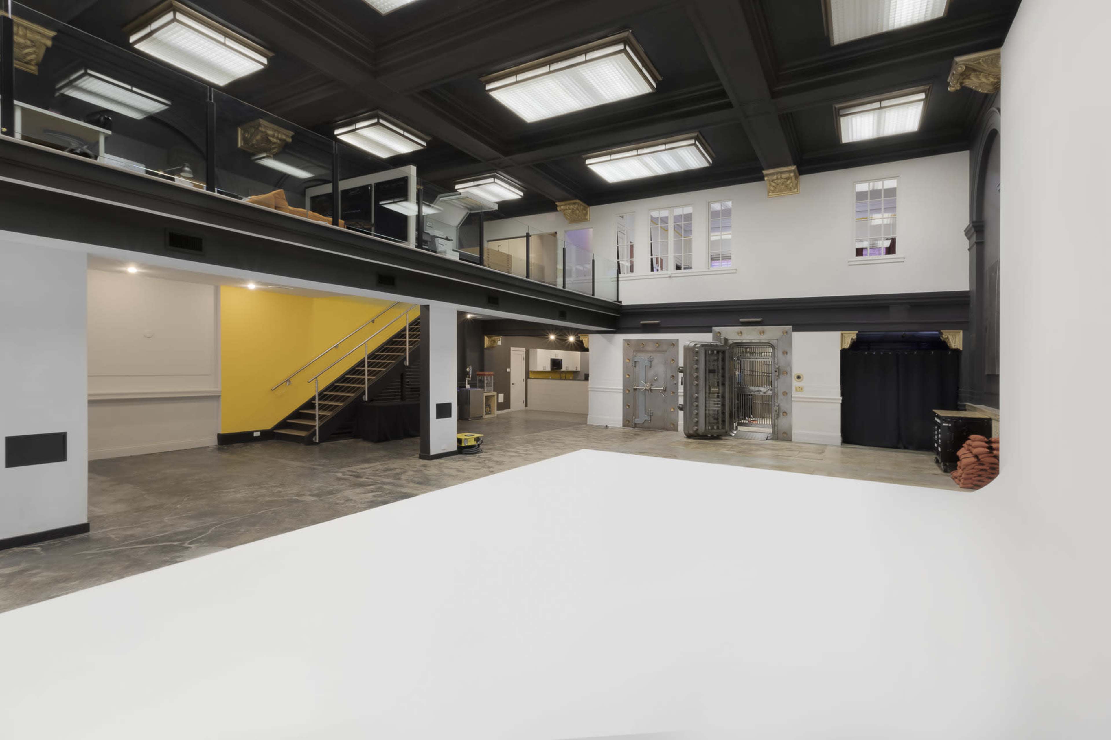 A spacious, modern interior of a building featuring an open upper level with a staircase, large windows, and a mix of textured walls and flooring.