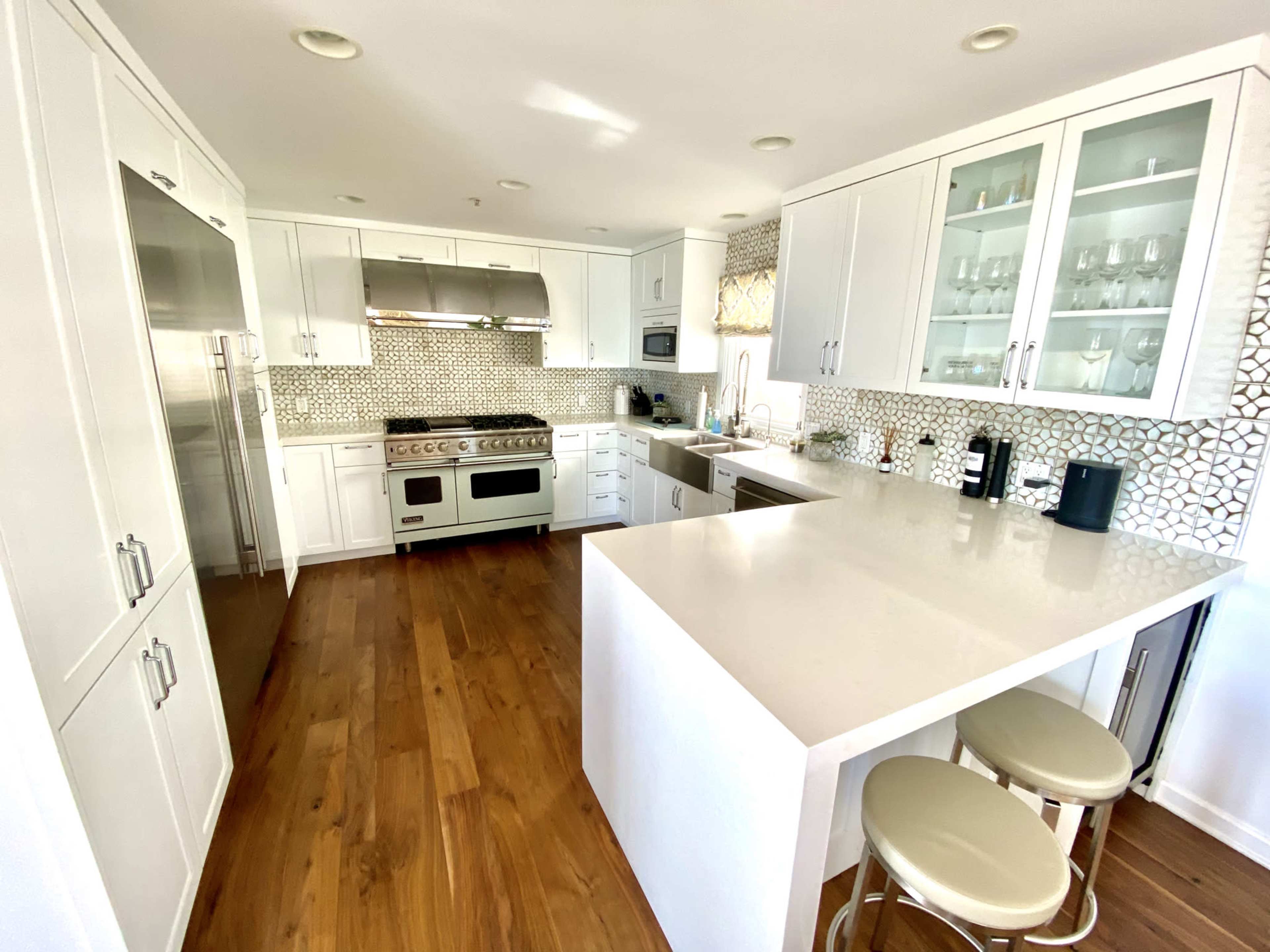 A modern kitchen featuring white cabinets, a large island with bar stools, and a backsplash made of geometric tiles.