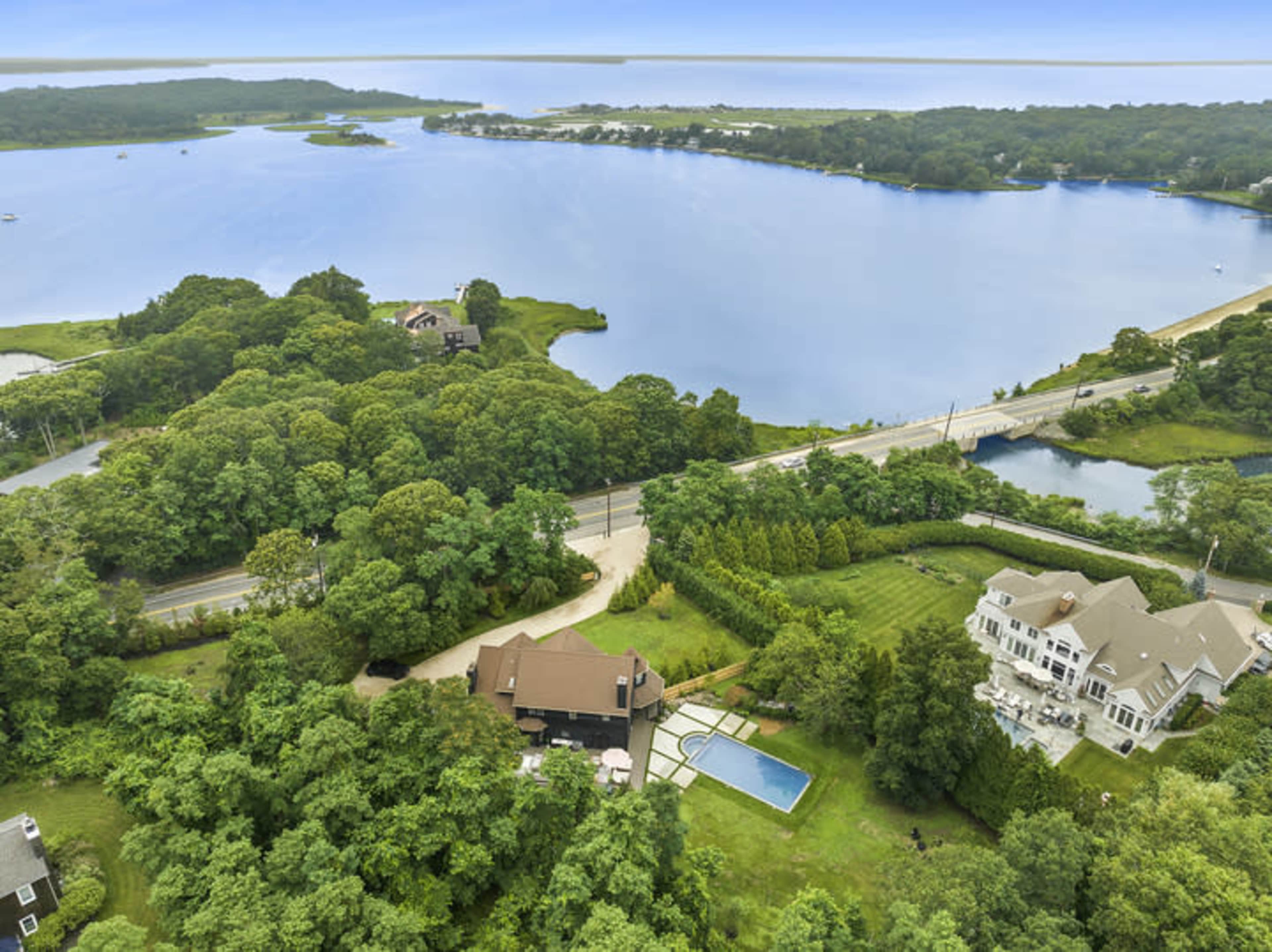 The aerial view shows a large body of water surrounded by lush greenery, with several homes and a road nearby.