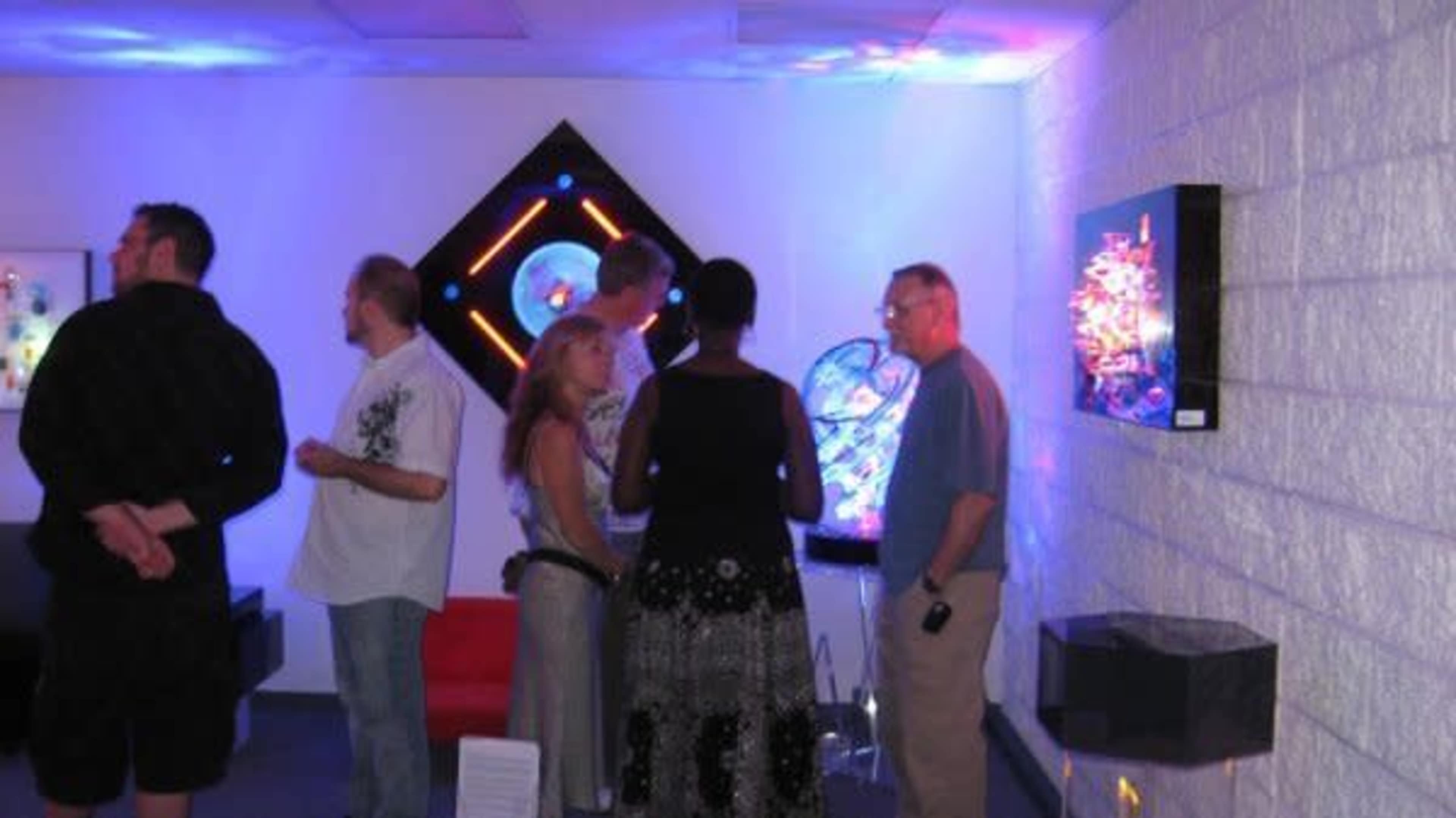 A group of people stands and converses in an art gallery with colorful lights and various artworks displayed on the walls.