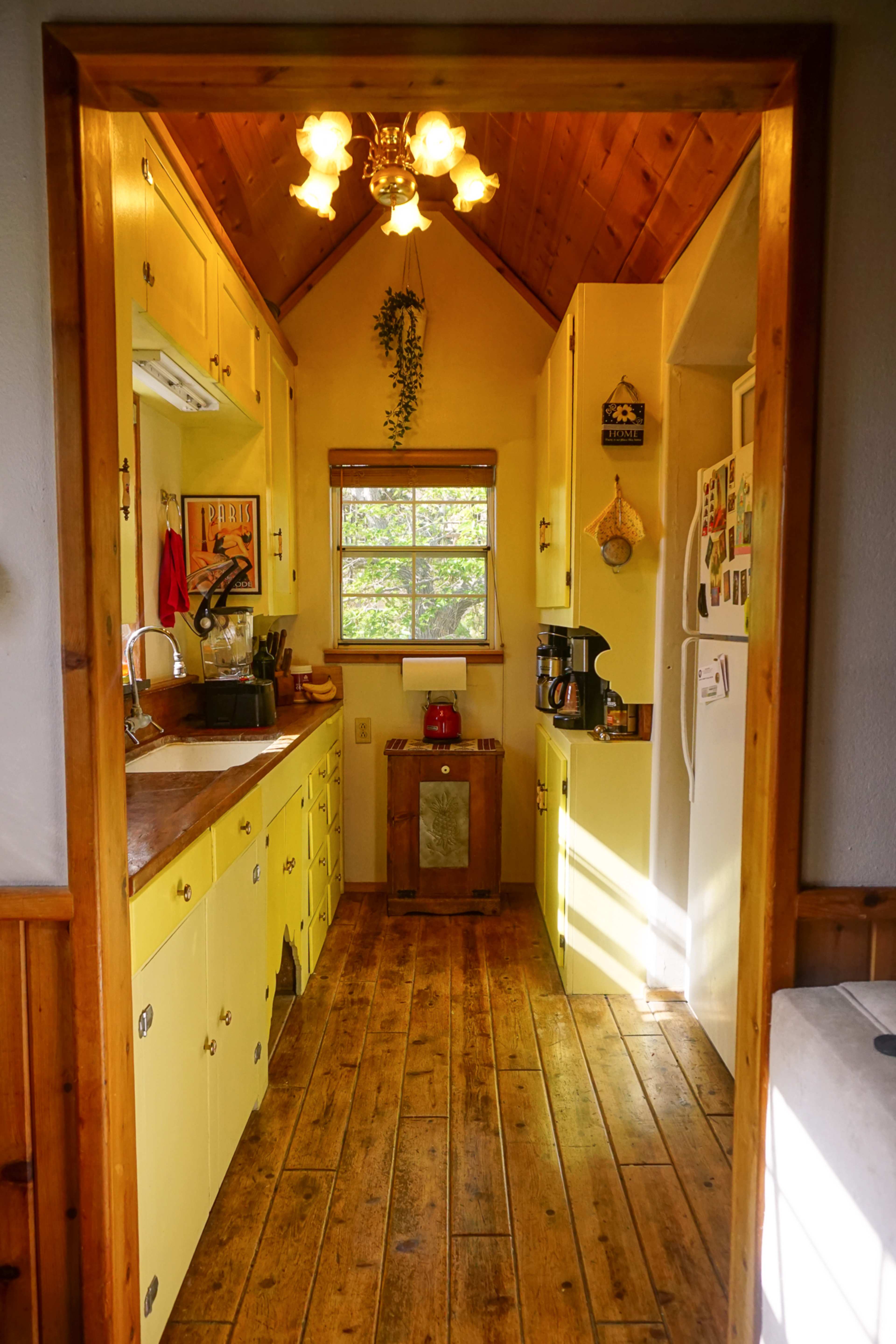 A brightly lit kitchen features yellow cabinets, wooden flooring, and a window with natural light streaming in.