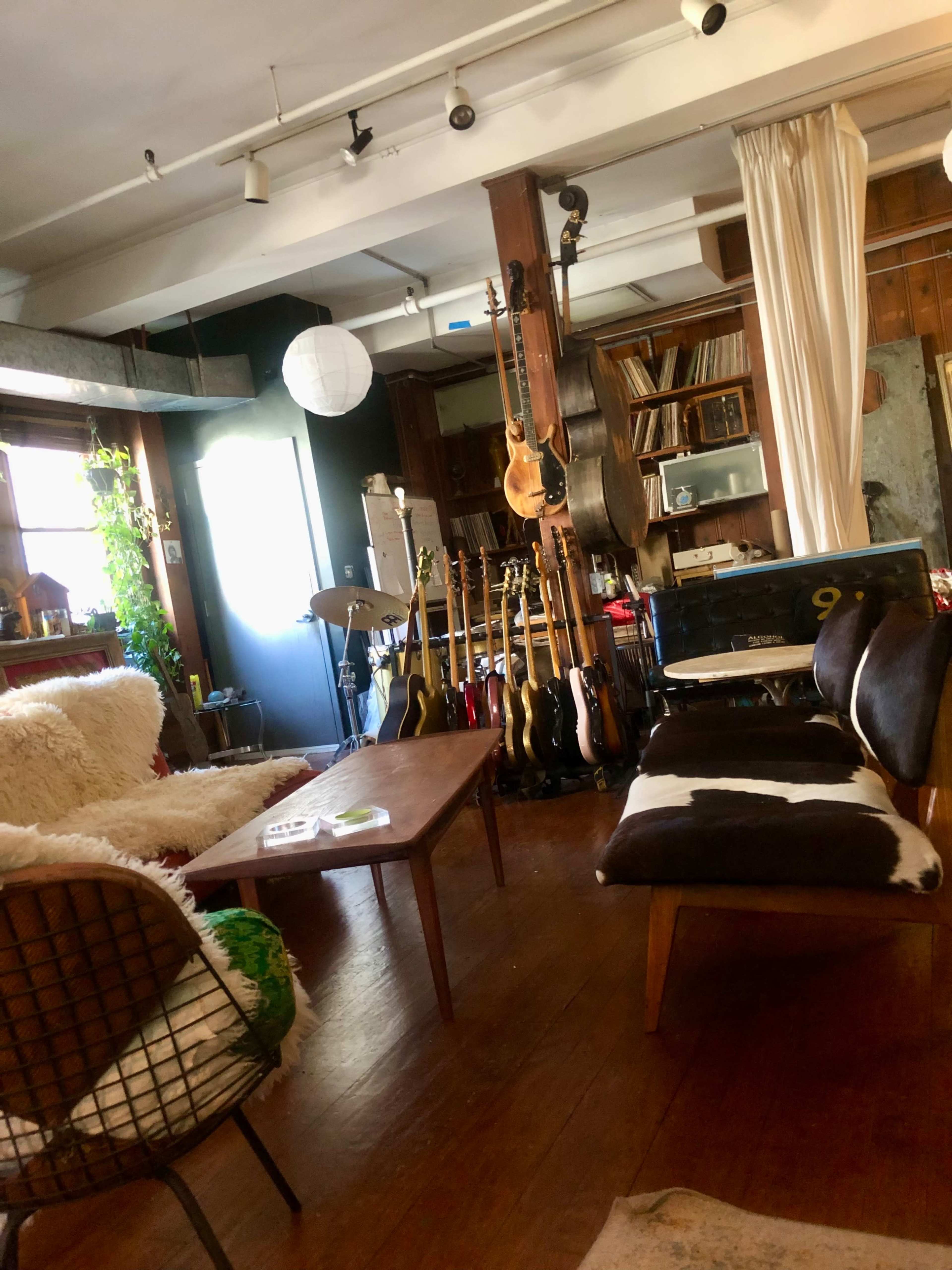 A cozy living space with a wooden floor, a low coffee table, a white rug, and various guitars displayed along the wall.