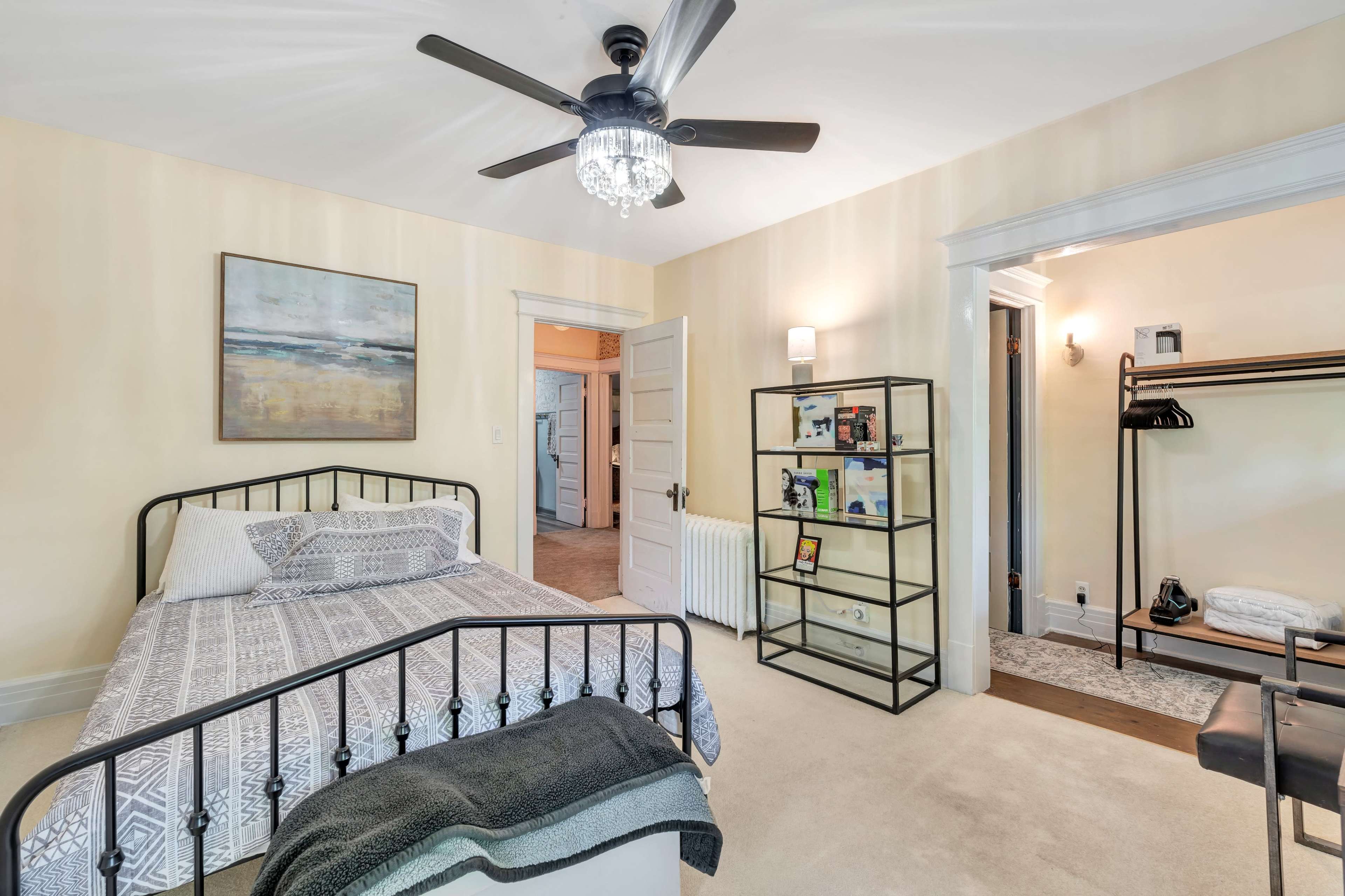 A bedroom with a metal bed frame, a bookshelf, and a walk-in closet area, featuring neutral-colored walls and a ceiling fan.