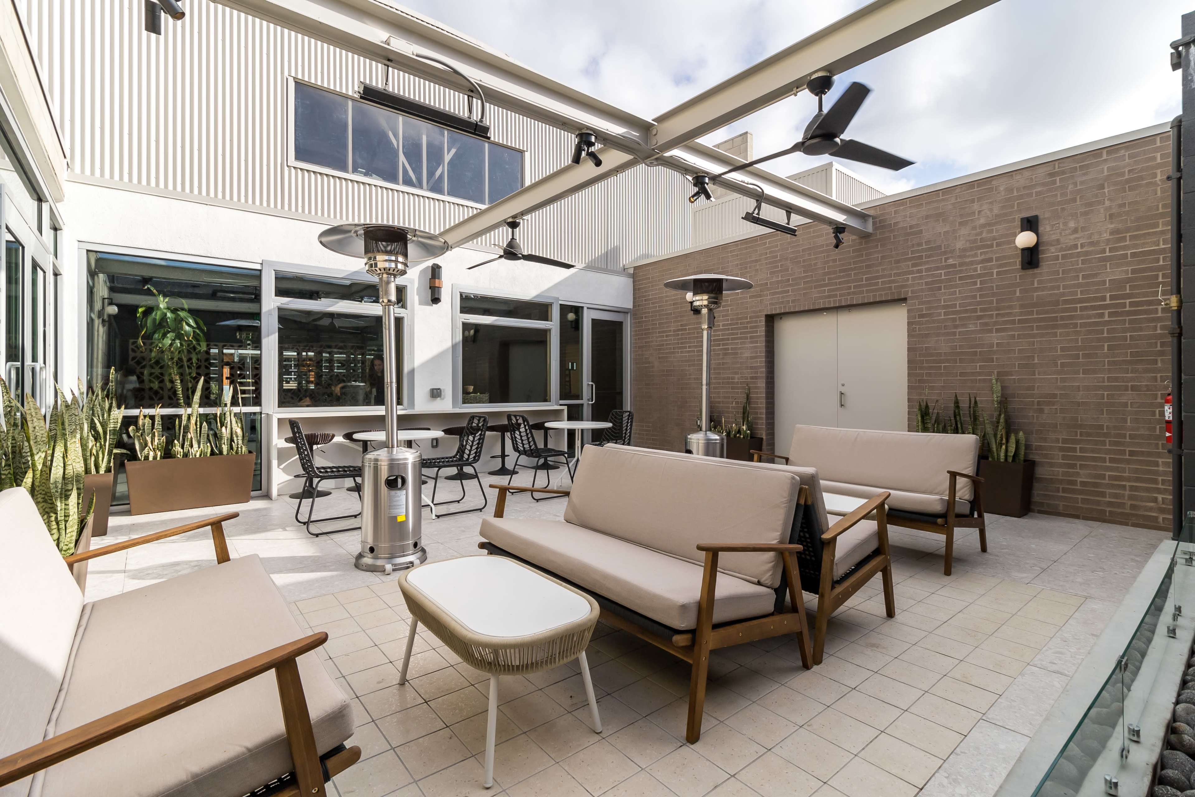 A spacious outdoor patio area with lounge seating, heating lamps, and a few potted plants.