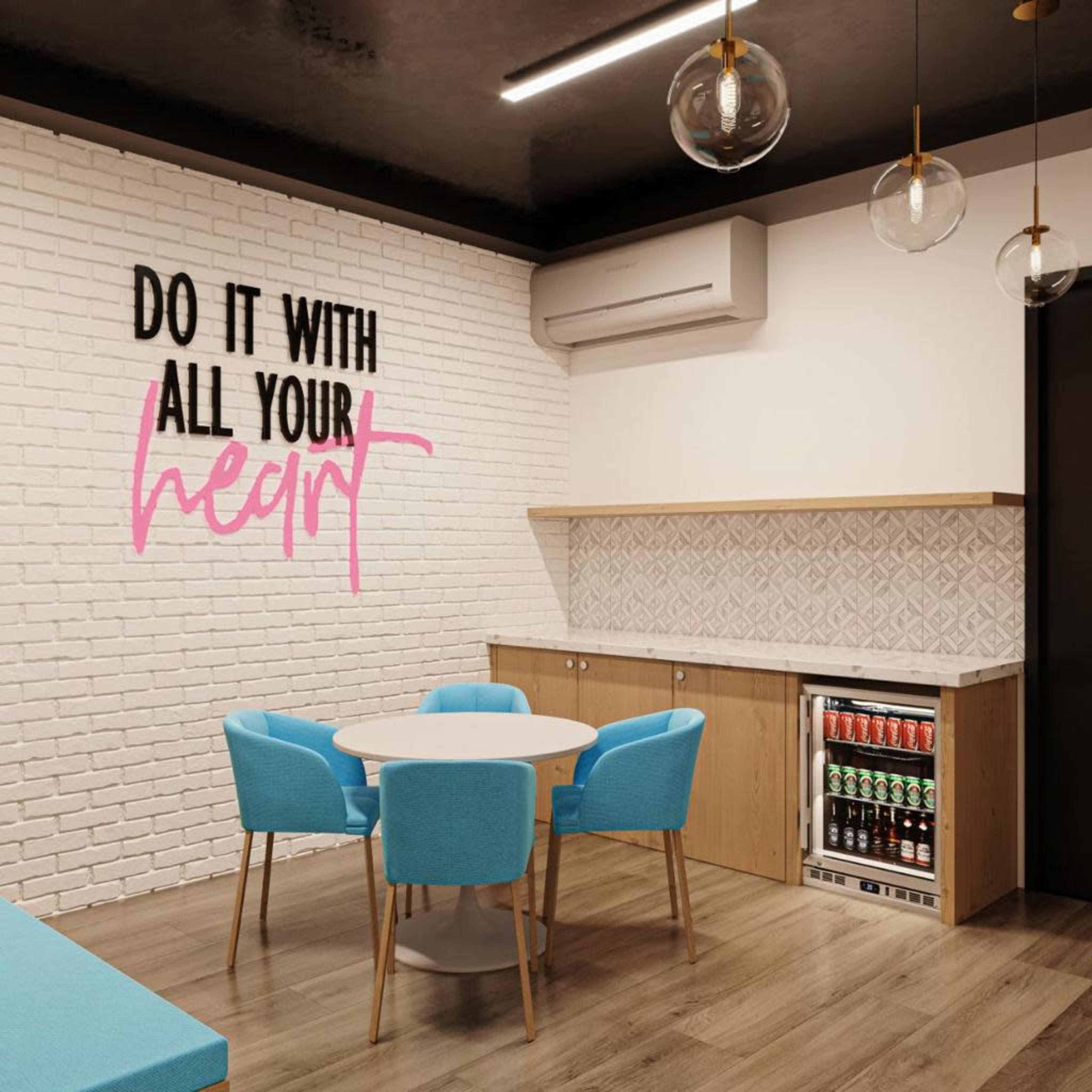 A modern break room features a round table with turquoise chairs, a decorative wall with motivational text, and a kitchenette with a small beverage fridge.