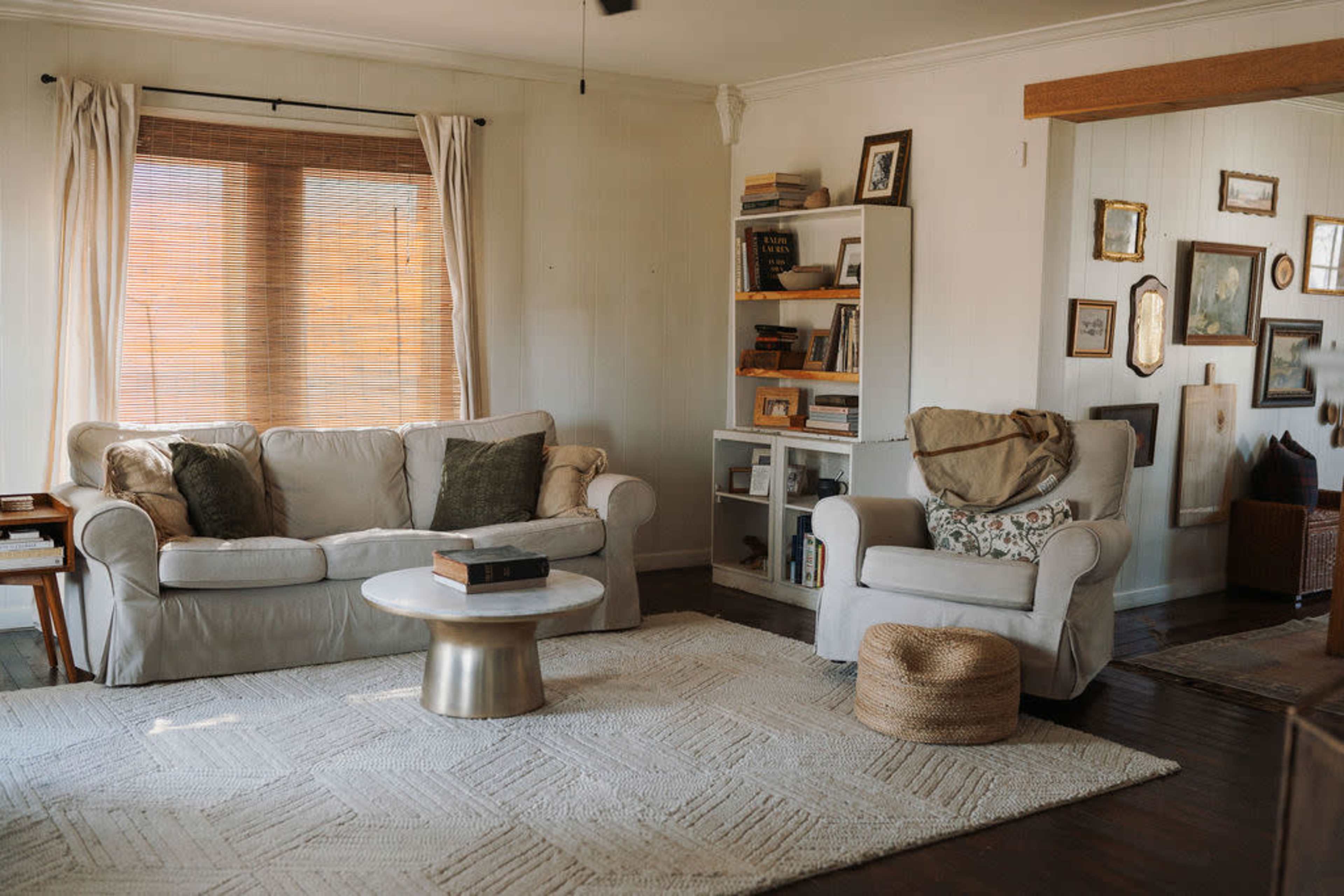 The living room features a light-colored sofa, a round coffee table, a bookshelf filled with books, and a natural fiber rug.