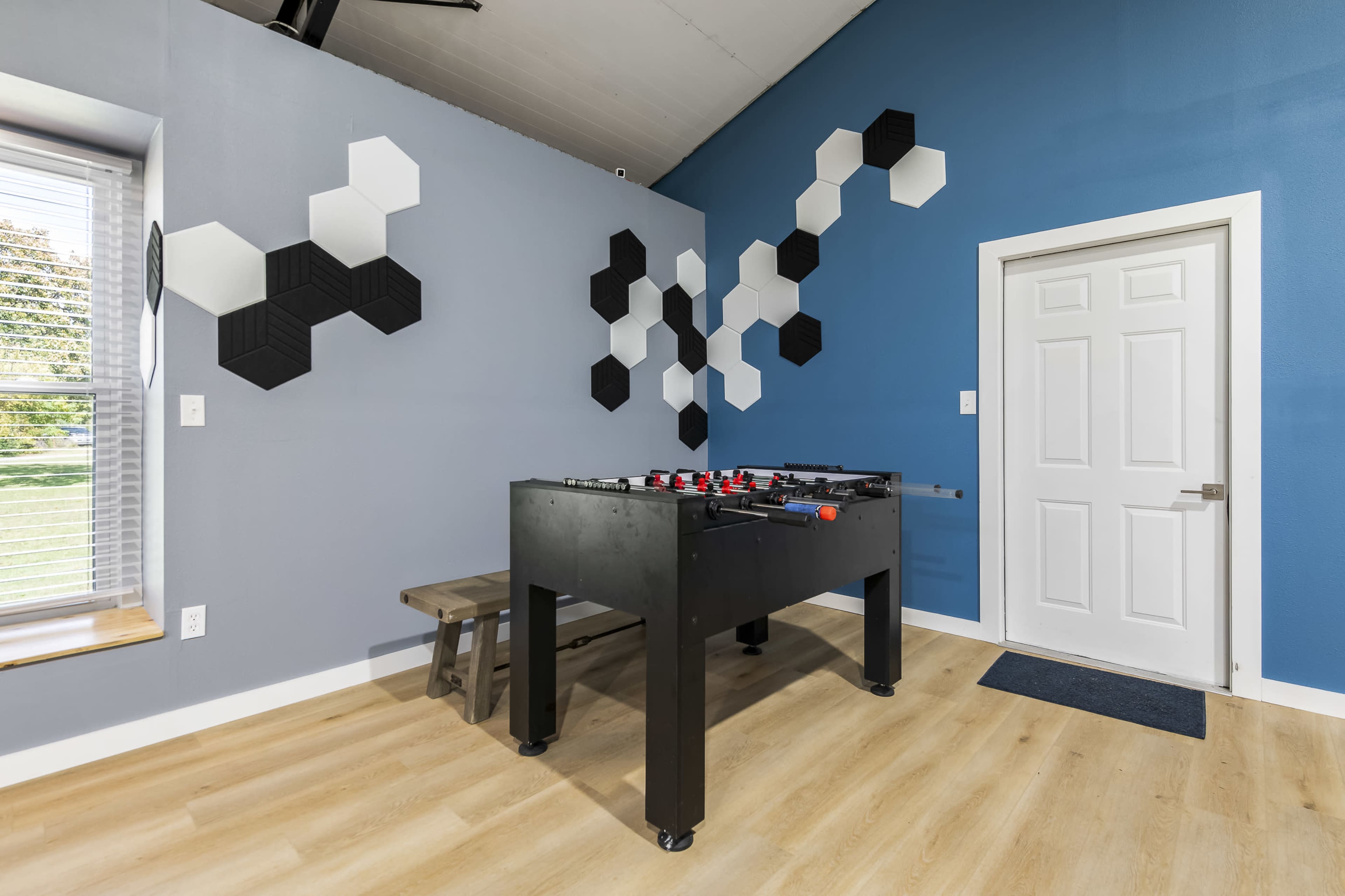 A foosball table is positioned in a well-lit room with blue walls, adjacent to a white door and a bench.