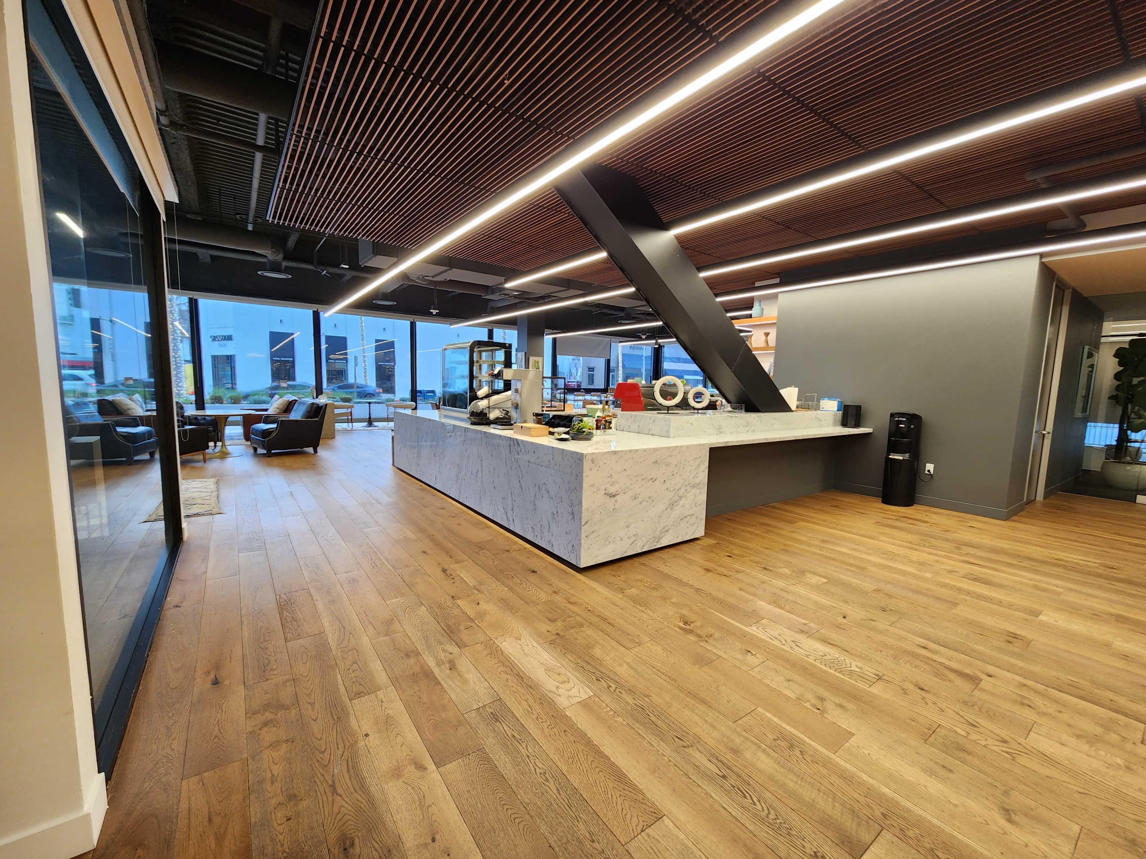 A modern office interior featuring a spacious reception area with a marble counter, wooden flooring, and large windows.