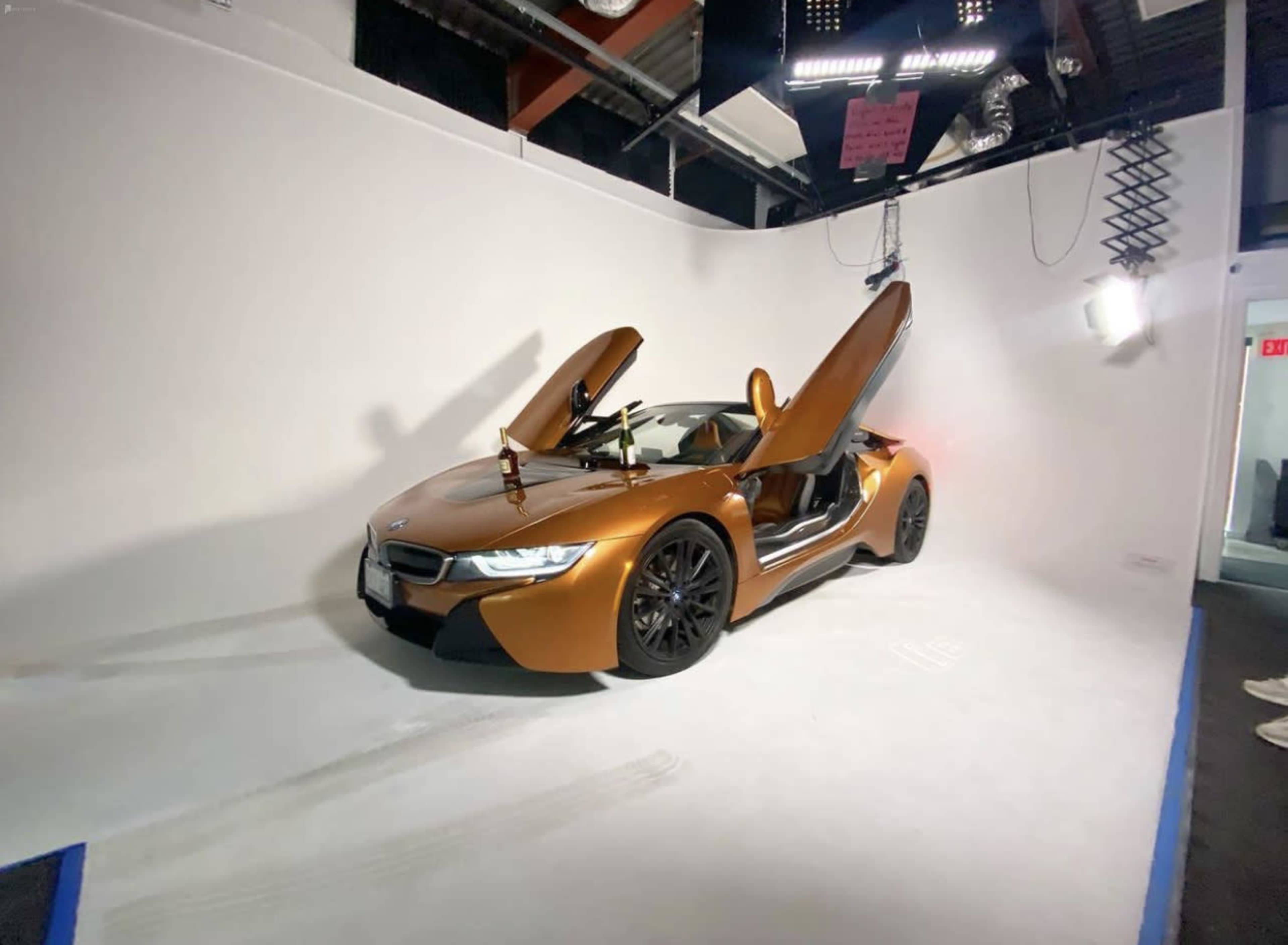 A bronze BMW i8 sports car with its doors open in a well-lit studio setting.