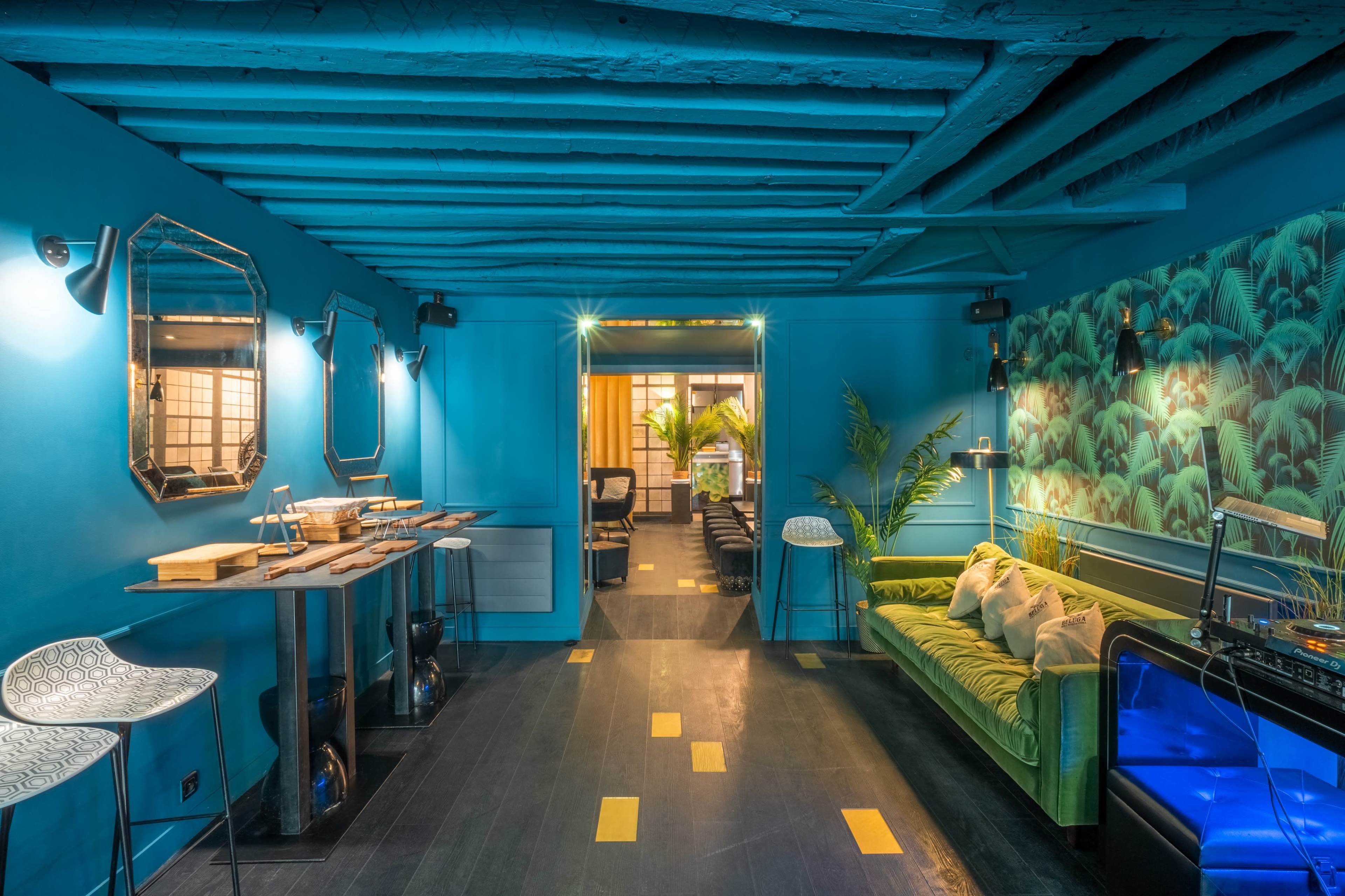 A brightly colored room with blue walls, a green sofa, and a mix of modern furniture, illuminated by soft lighting and featuring plants in the background.