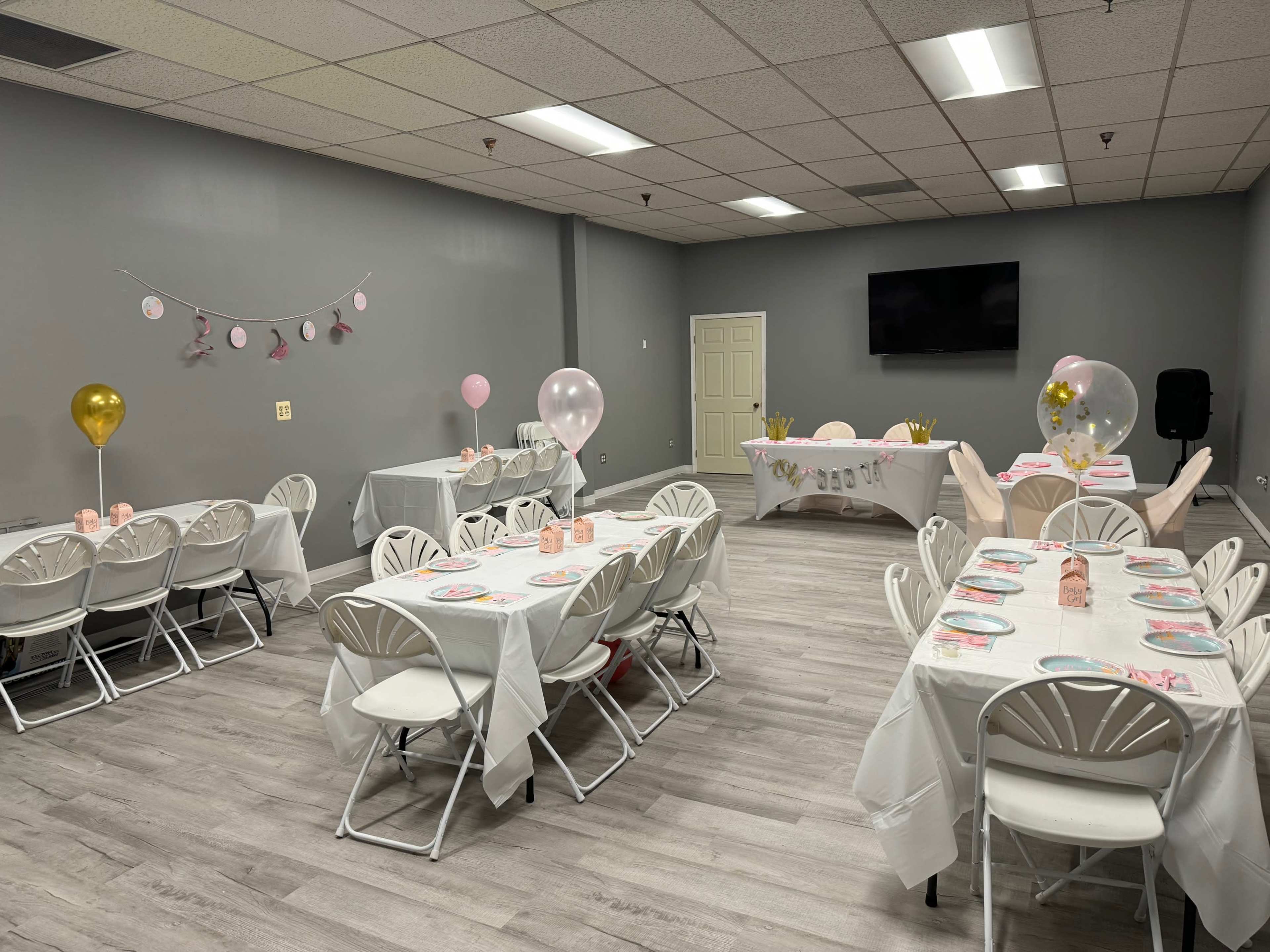 A banquet room set up for a celebration, featuring multiple tables adorned with pink and gold decorations, balloons, and place settings.