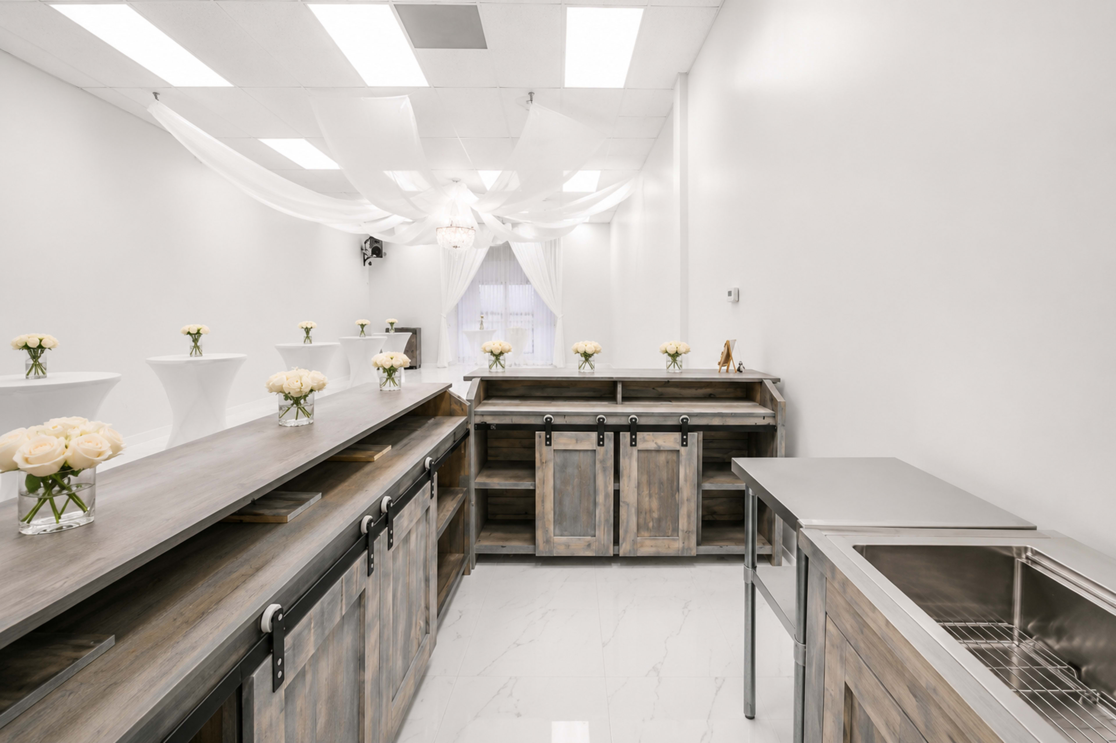 The image features a minimalist interior space with wooden counters, white floral arrangements on display, and draped fabric overhead.