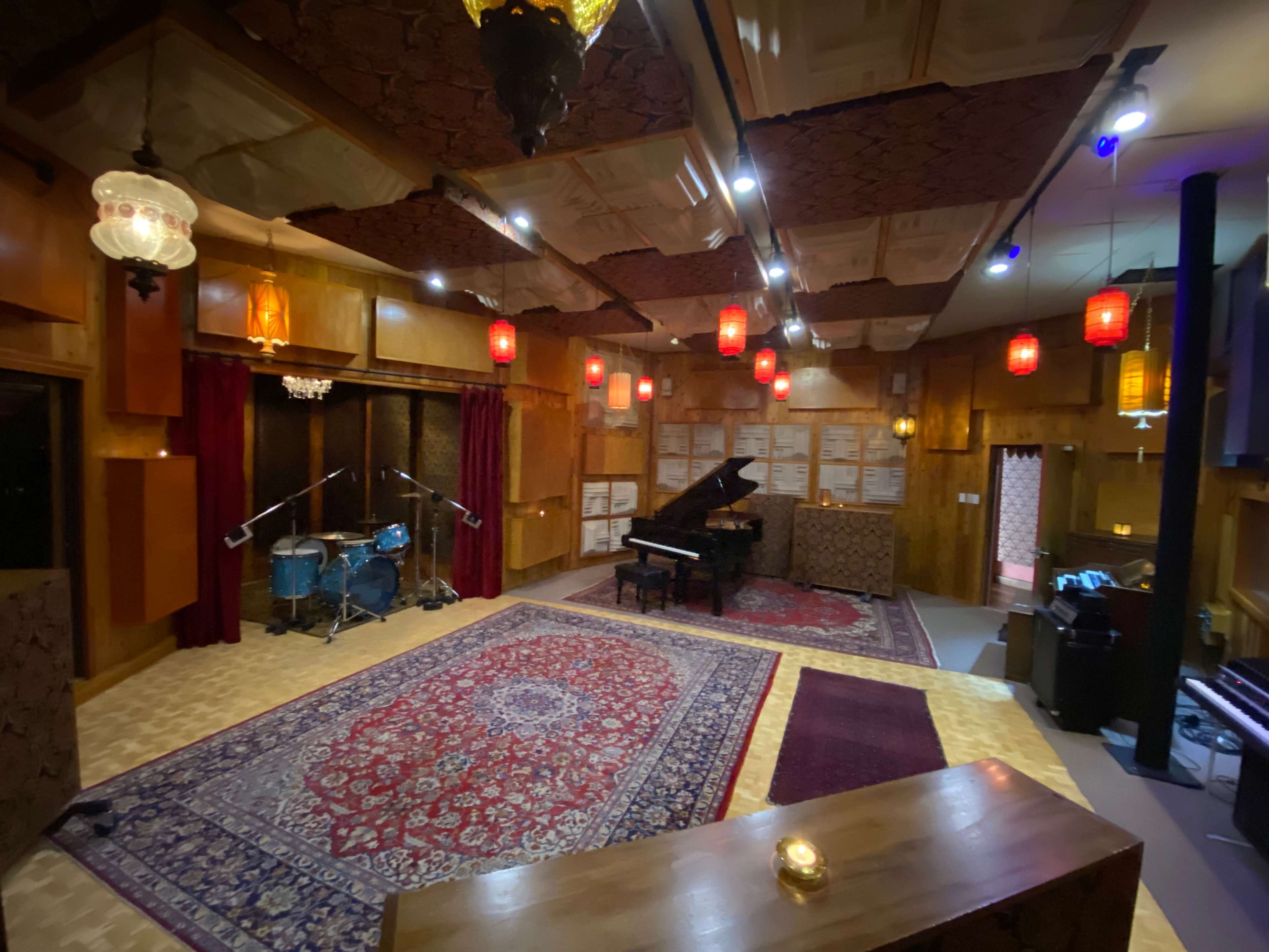 A music studio featuring a grand piano, a drum set, and ambient lighting with decorative lanterns.
